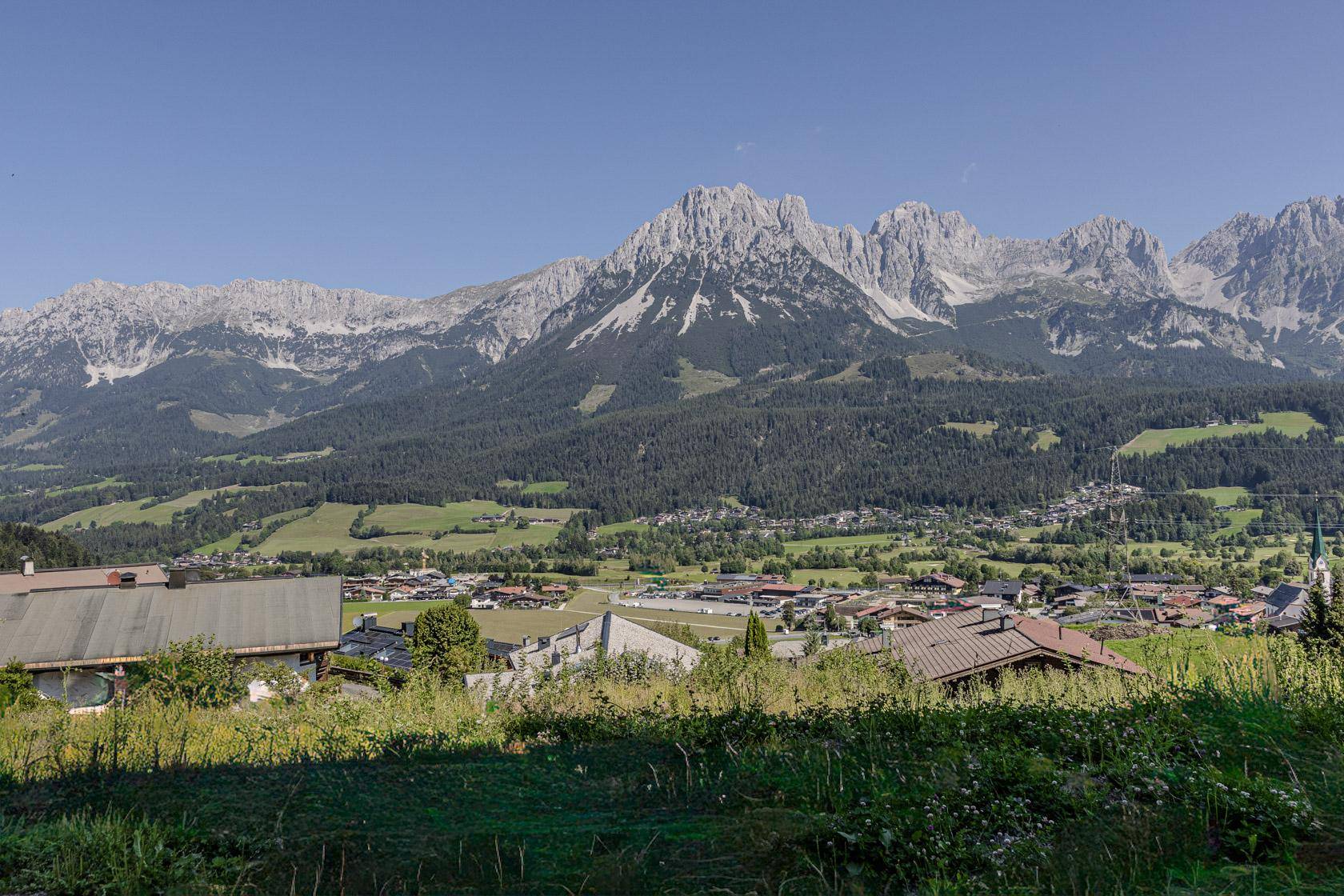 Weitläufiger Blick über ein malerisches Tal mit traditionellen Häusern und imposanten Berggipfeln.