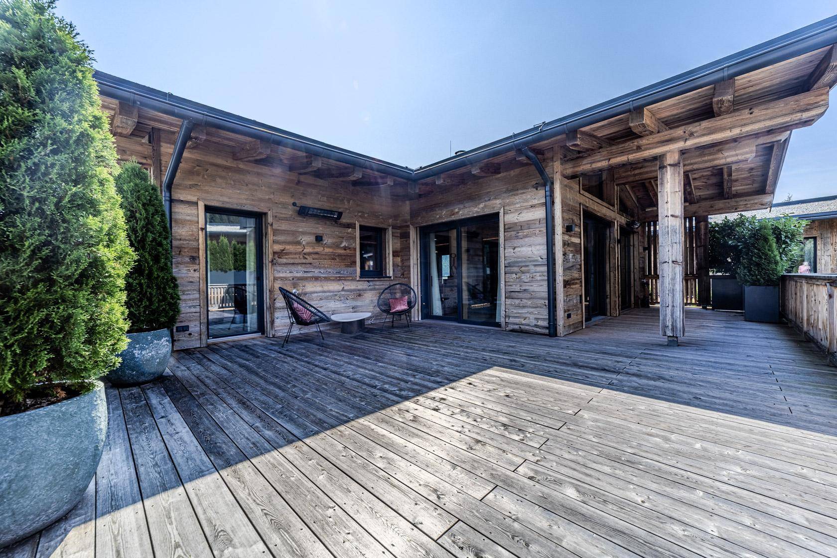 Weitläufige Holzterrasse mit Sitzgelegenheiten und Zugang zu den Innenräumen des Hauses.