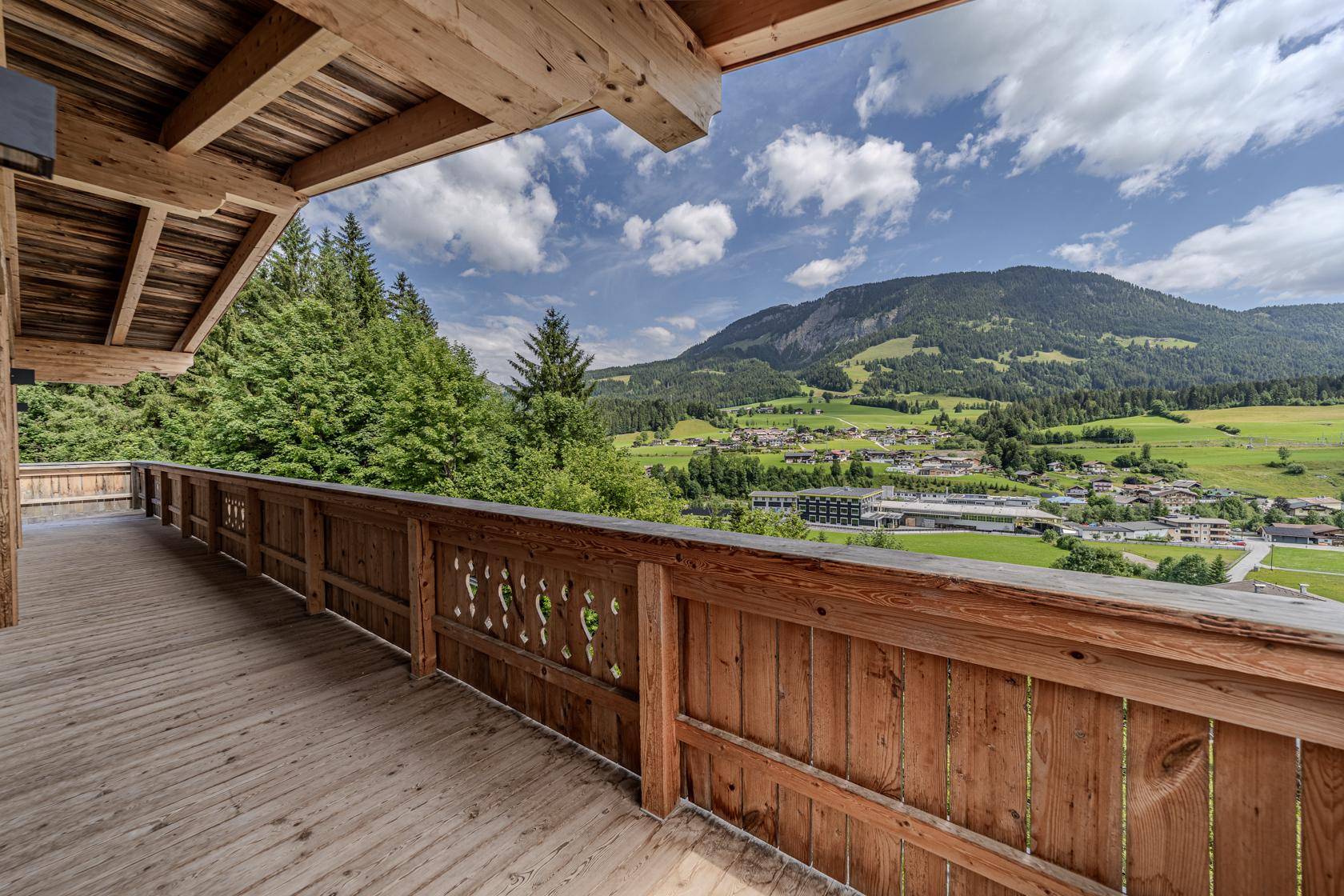 Geräumiger Holzbalkon mit traditionellem Geländer und weitem Blick über das Tal und die Berge.