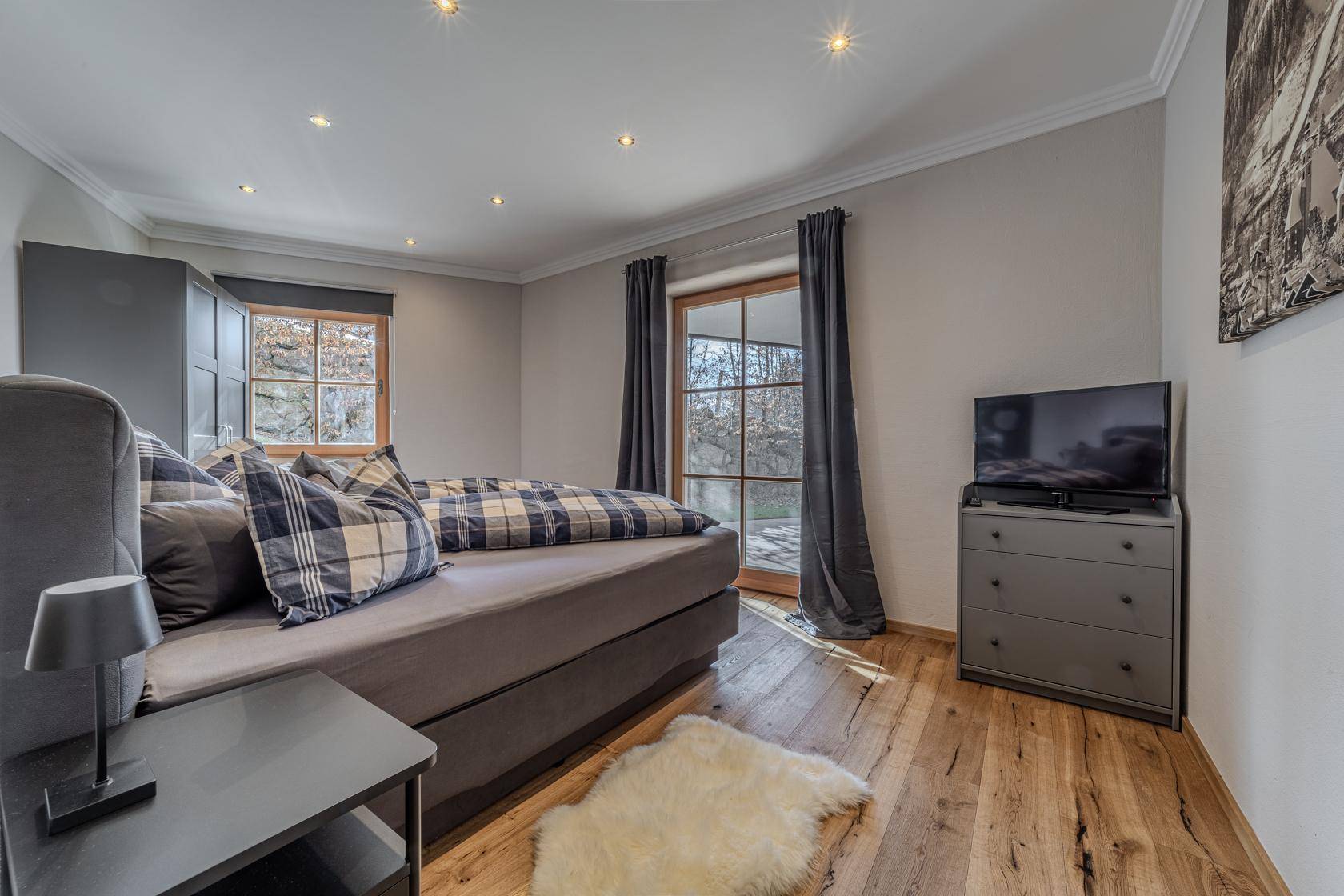Modernes Schlafzimmer mit Holzboden, bequemen Bett und Fenster mit Blick ins Grüne.