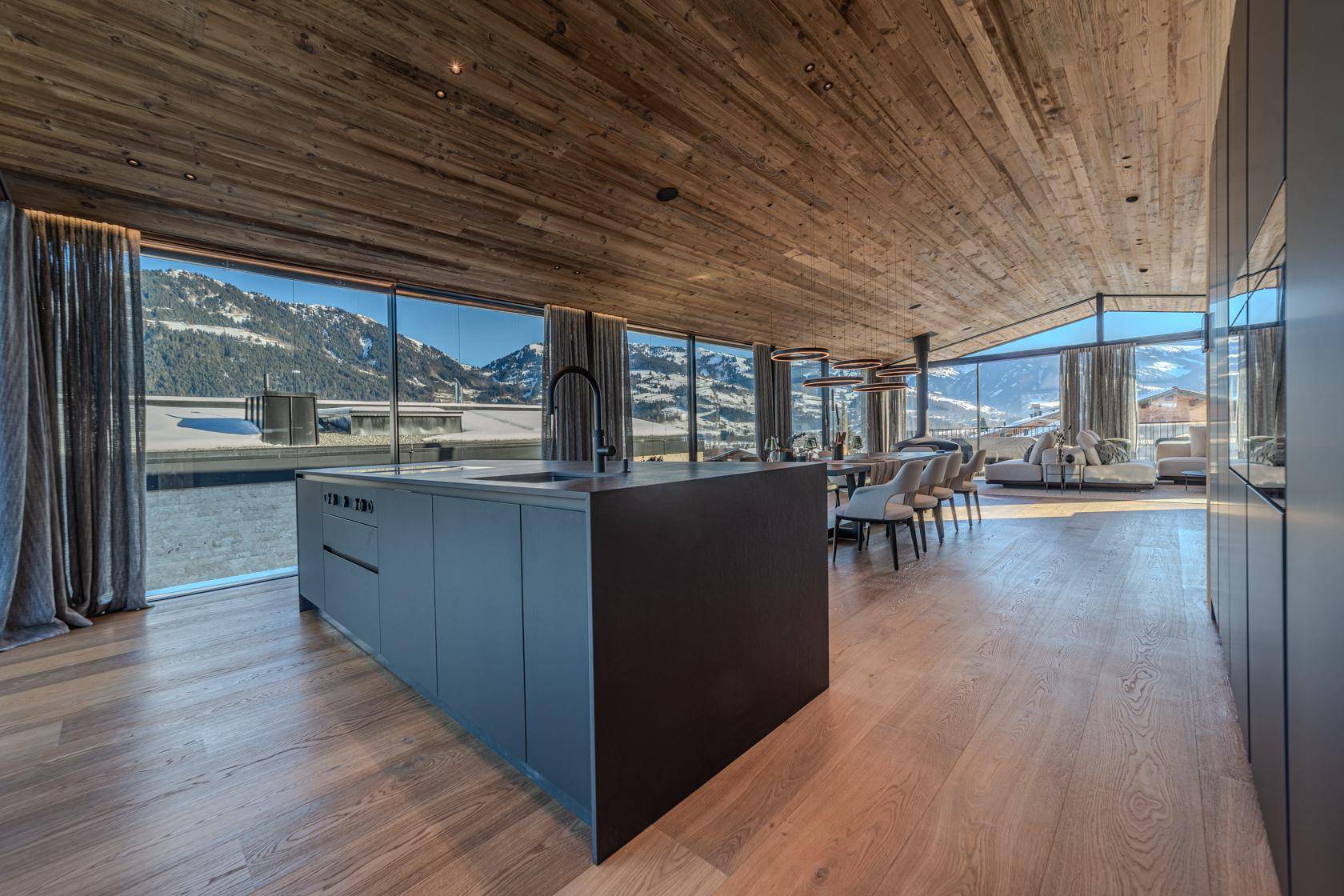 Elegante offene Küche mit dunkler Kücheninsel, Holzboden und Panoramafenstern mit Bergblick.