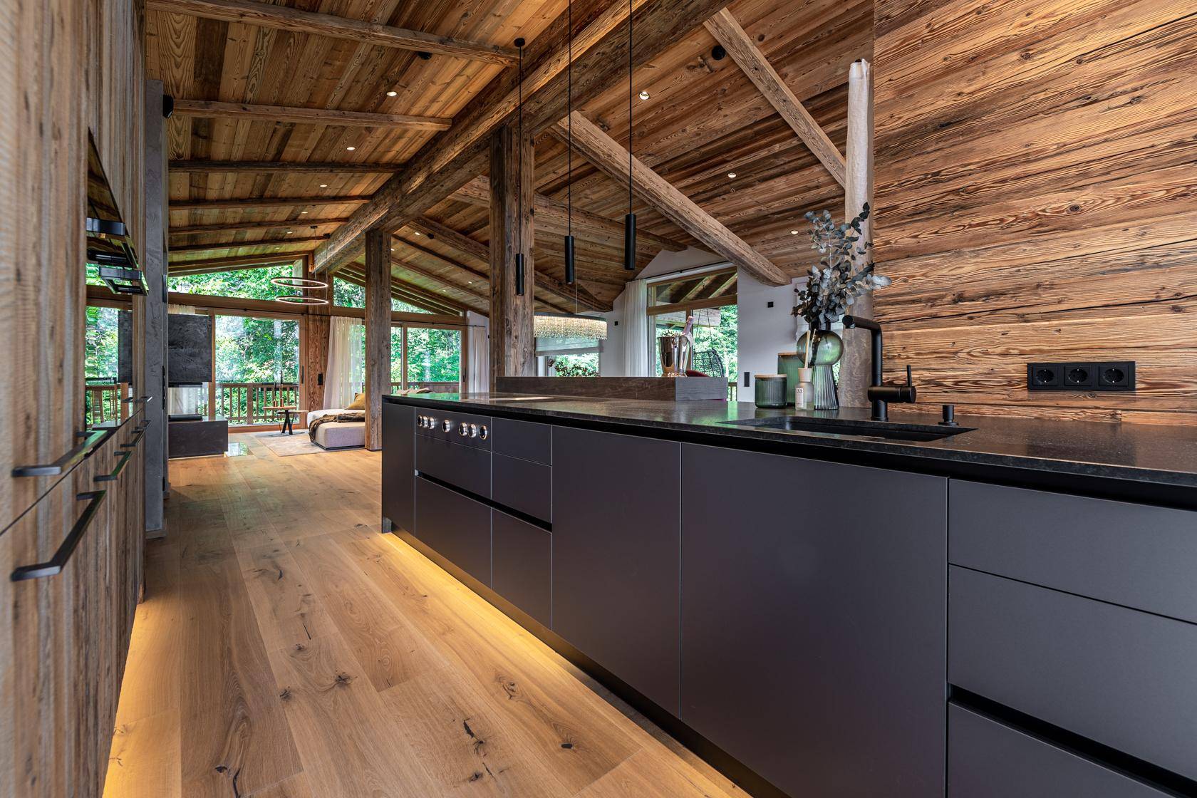 Moderne Küche mit dunkler Arbeitsplatte, integrierten Geräten und Holzwänden.