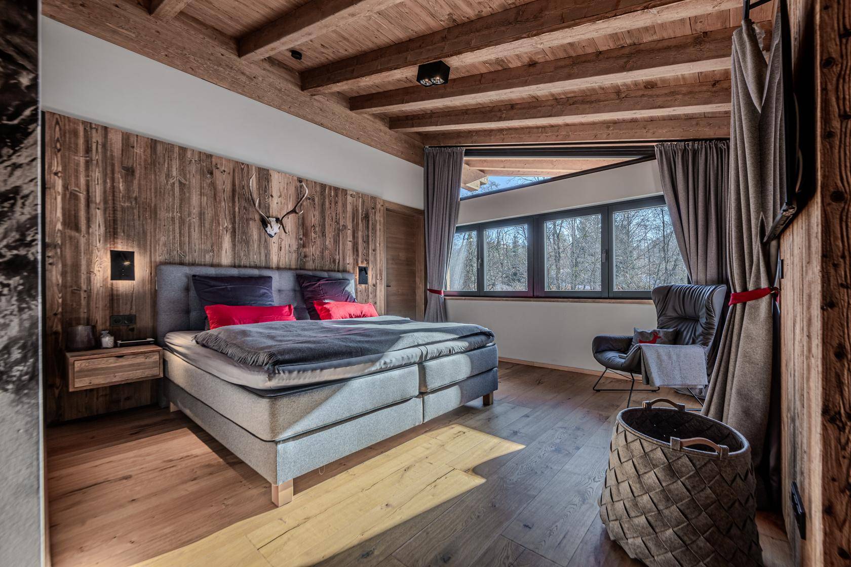 Schlafzimmer im Chalet-Stil mit Holzwand, großem Bett und Fenster mit Blick auf die Natur.