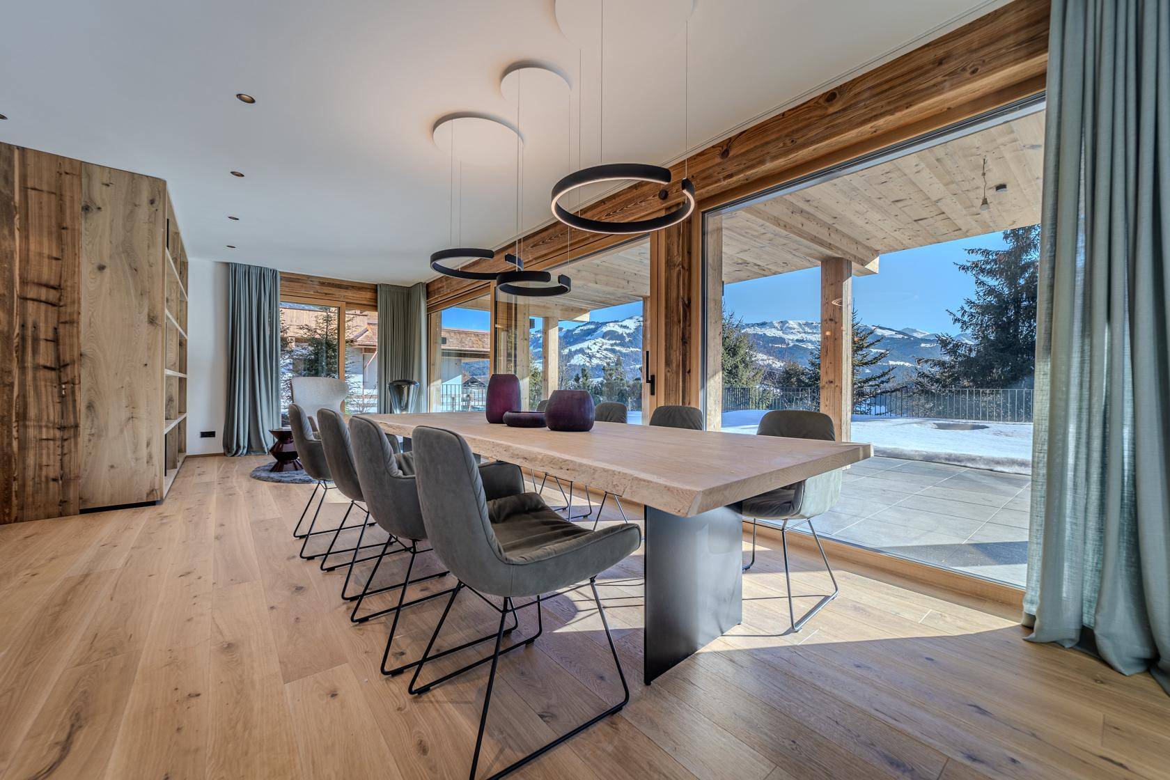 Heller Essbereich mit großem Holztisch, modernen Leuchten und Panoramablick auf die Berge.