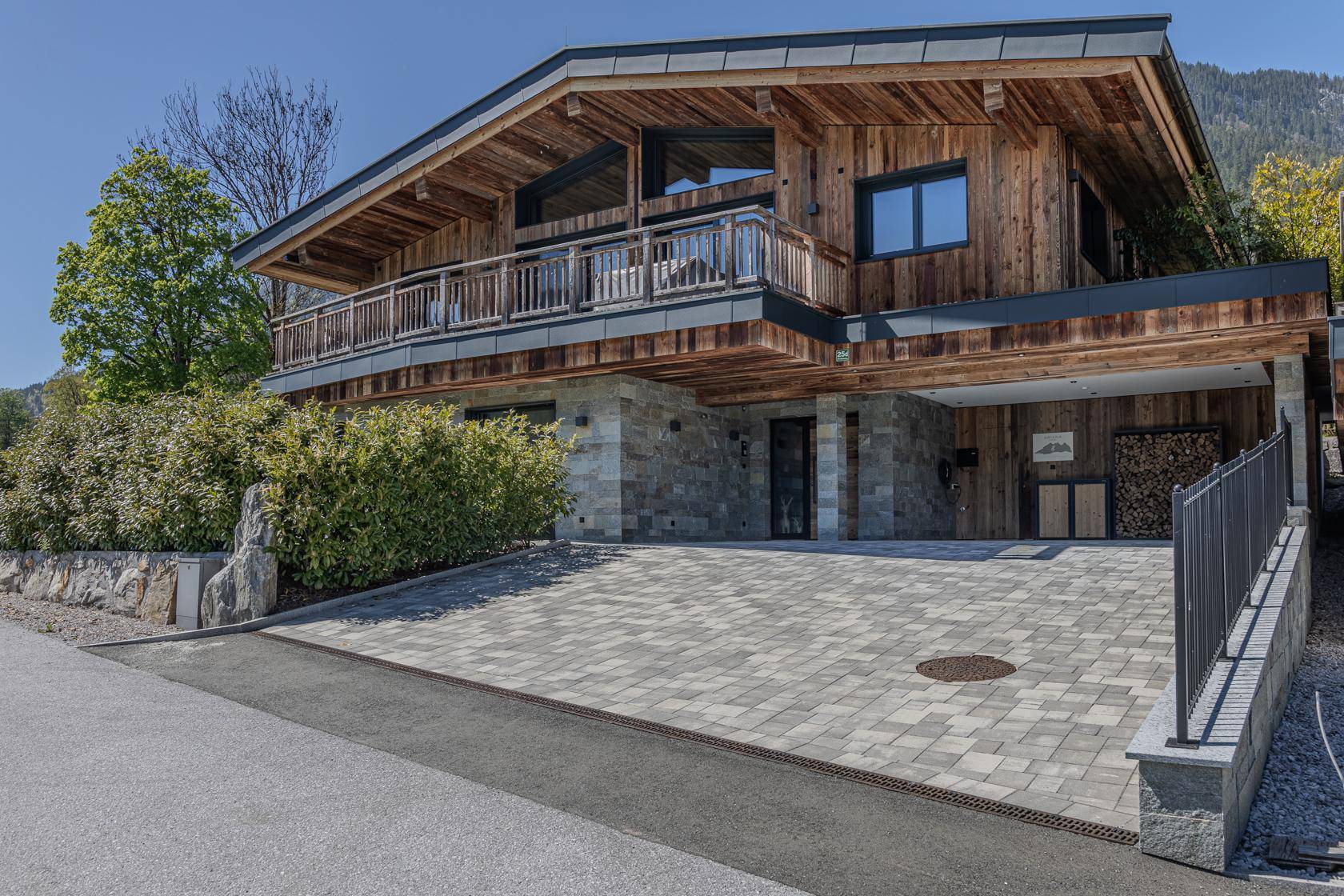 Attraktives Holzhaus im alpinen Stil mit Steinfassade, Balkon und gepflasterter Auffahrt.