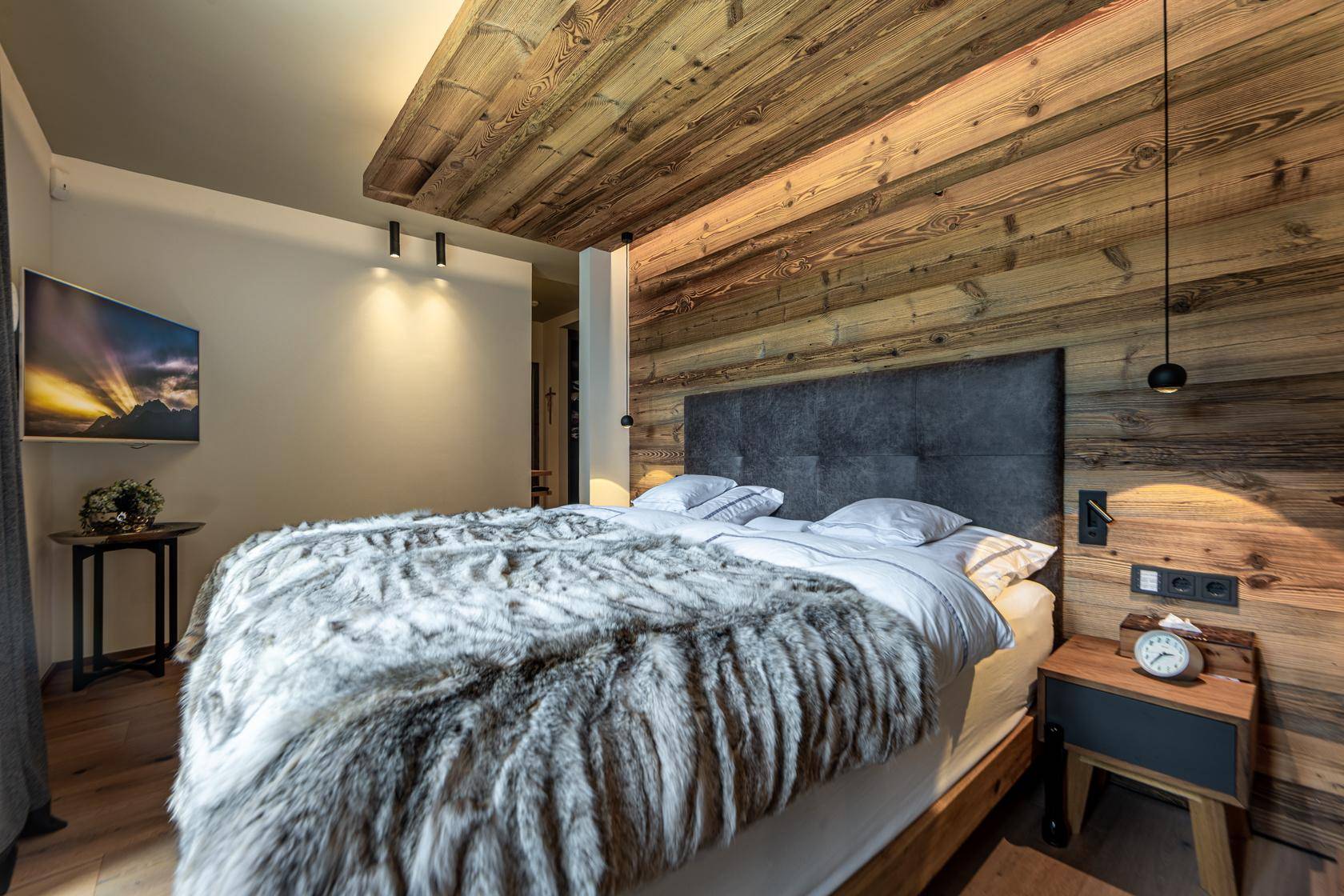 Gemütliches Schlafzimmer mit Holzwand, Holzbalkendecke und einem großen, einladenden Bett.