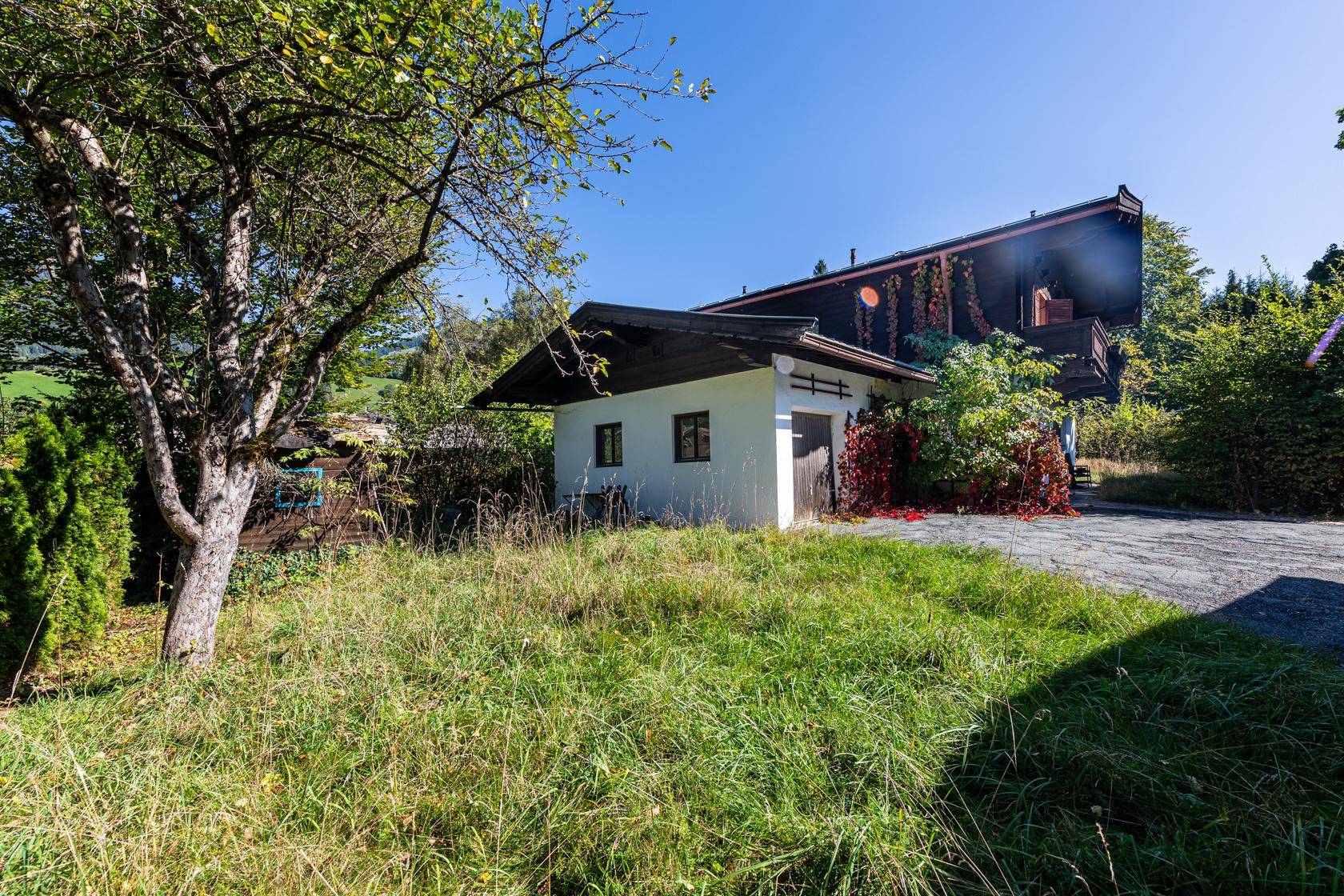 Kleines Nebengebäude in einem verwilderten Garten mit altem Obstbaum und Wiese.