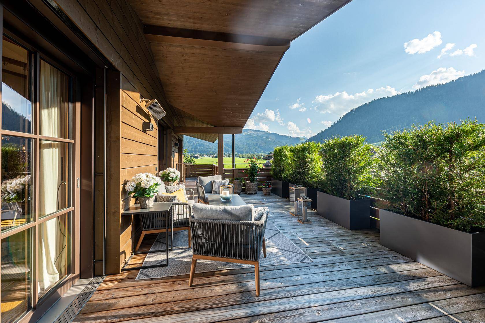 Weitläufige Holzterrasse mit Sitzgelegenheiten und Panoramablick auf die grüne Berglandschaft.