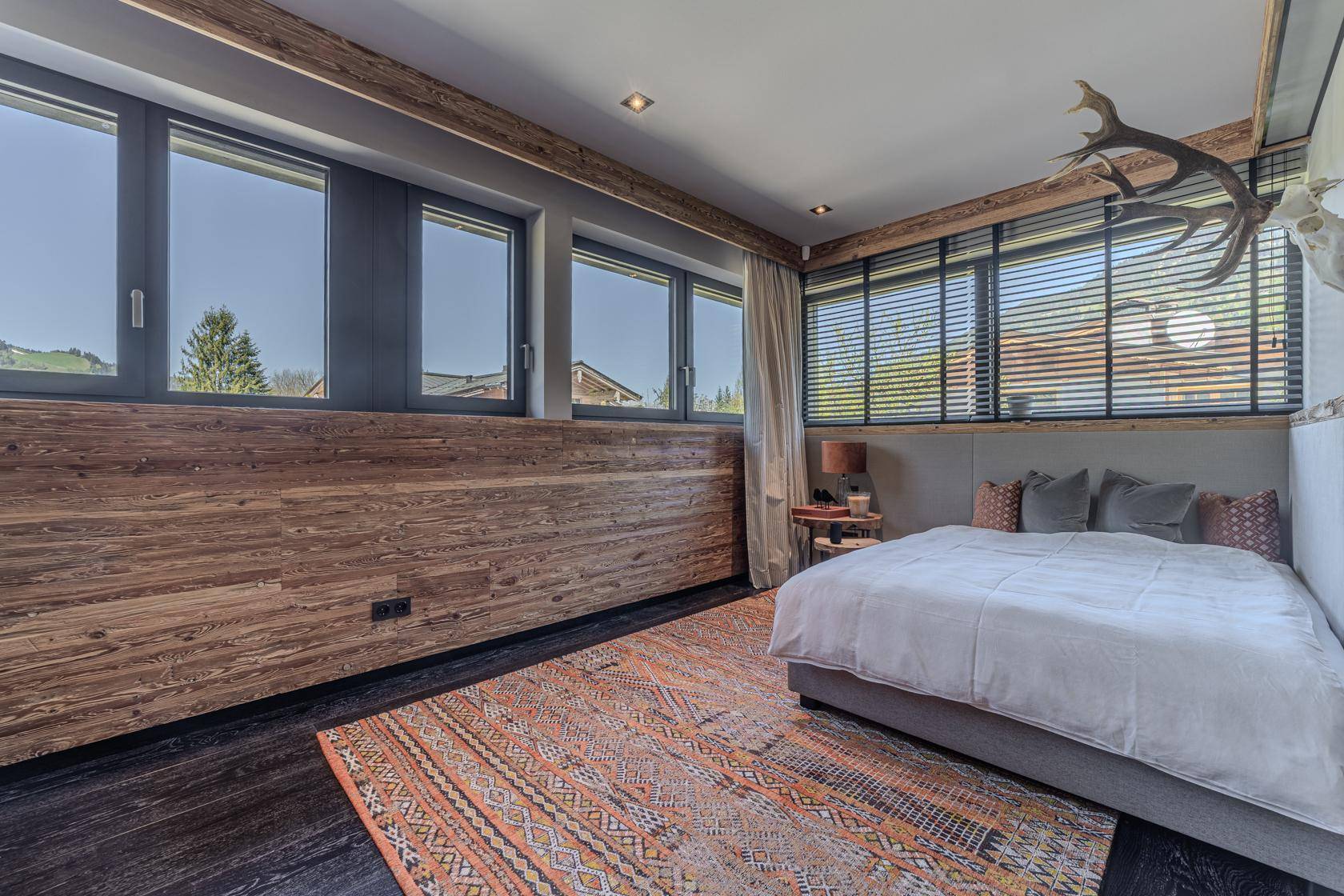 Gemütliches Schlafzimmer mit Holzwand, dunklem Boden und traditioneller Hirschgeweih-Dekoration.