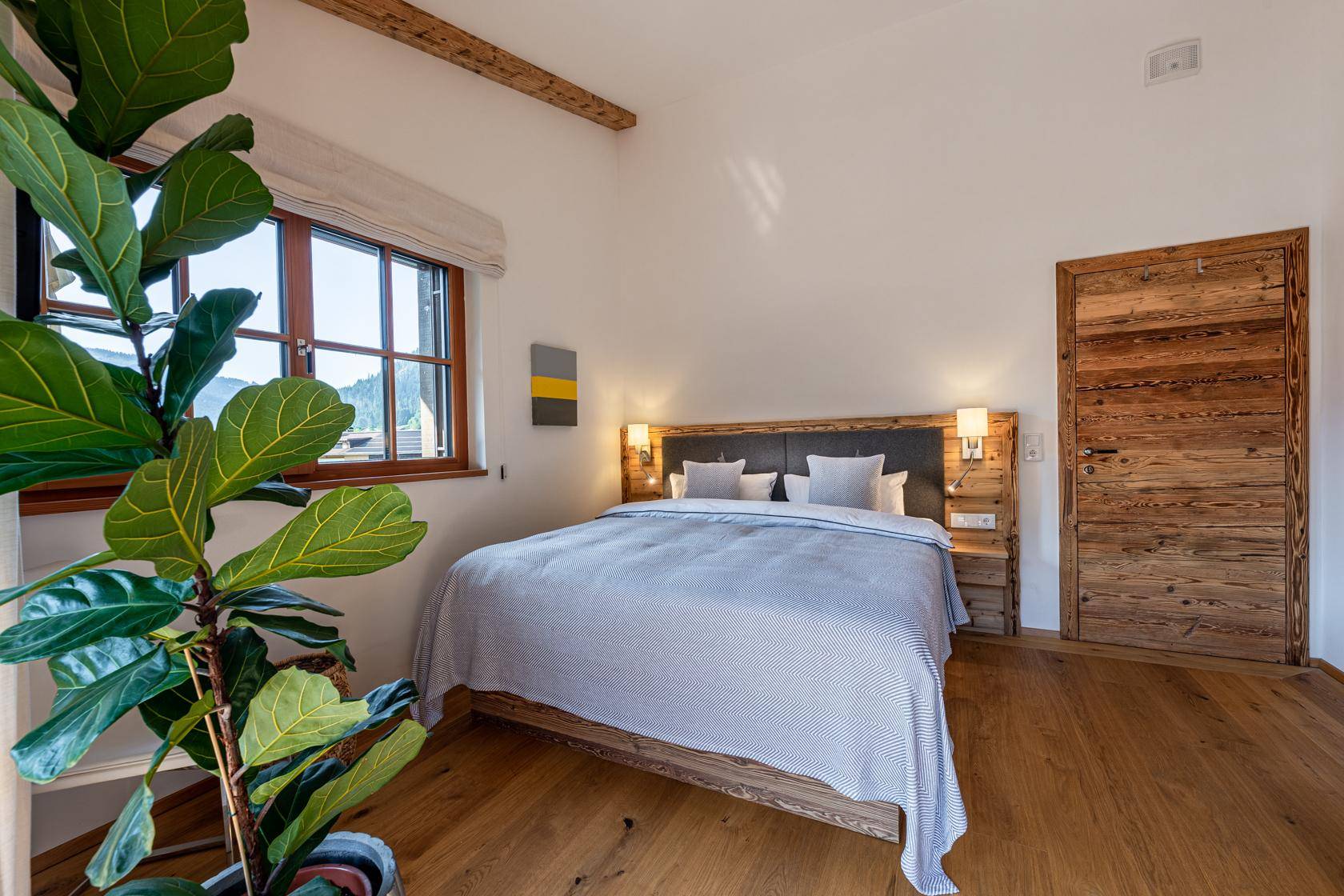 Gemütliches Schlafzimmer mit Holzboden, großem Fenster und Blick auf die Berglandschaft.