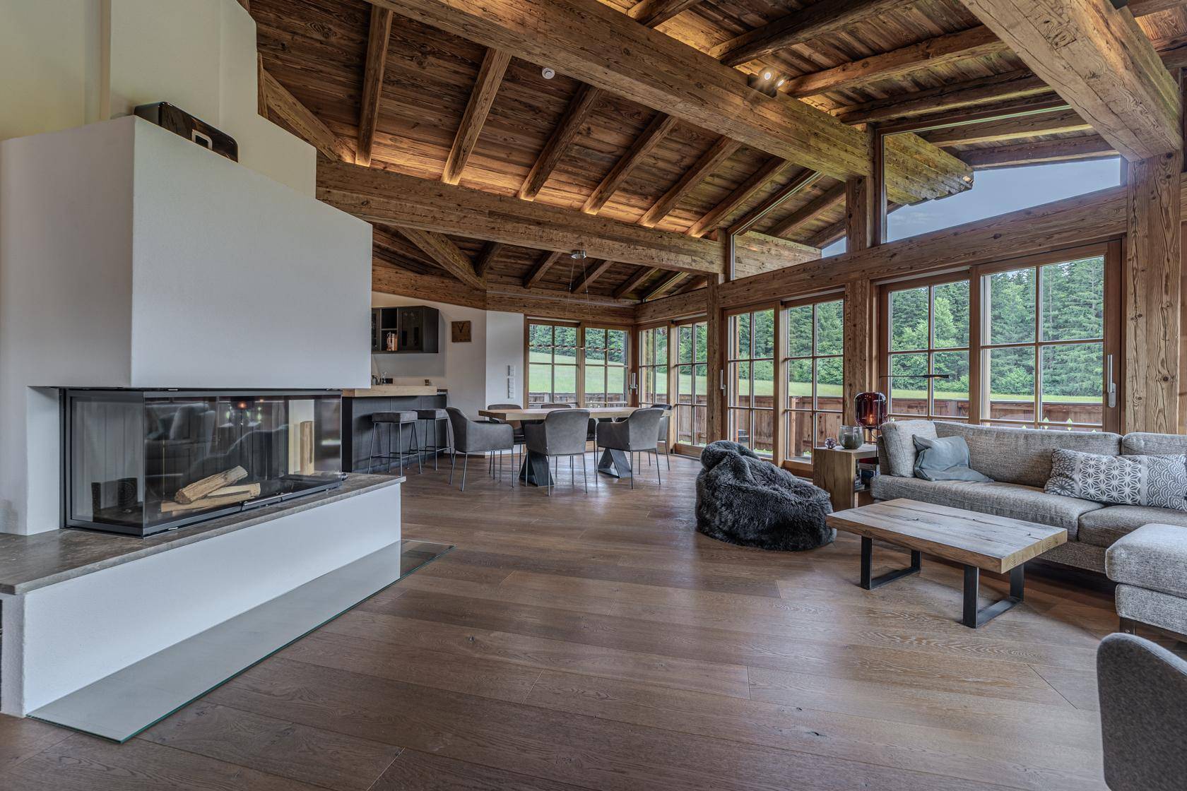 Geräumiger Wohnbereich mit modernem Kamin, Holzbalkendecke und großen Fenstern.