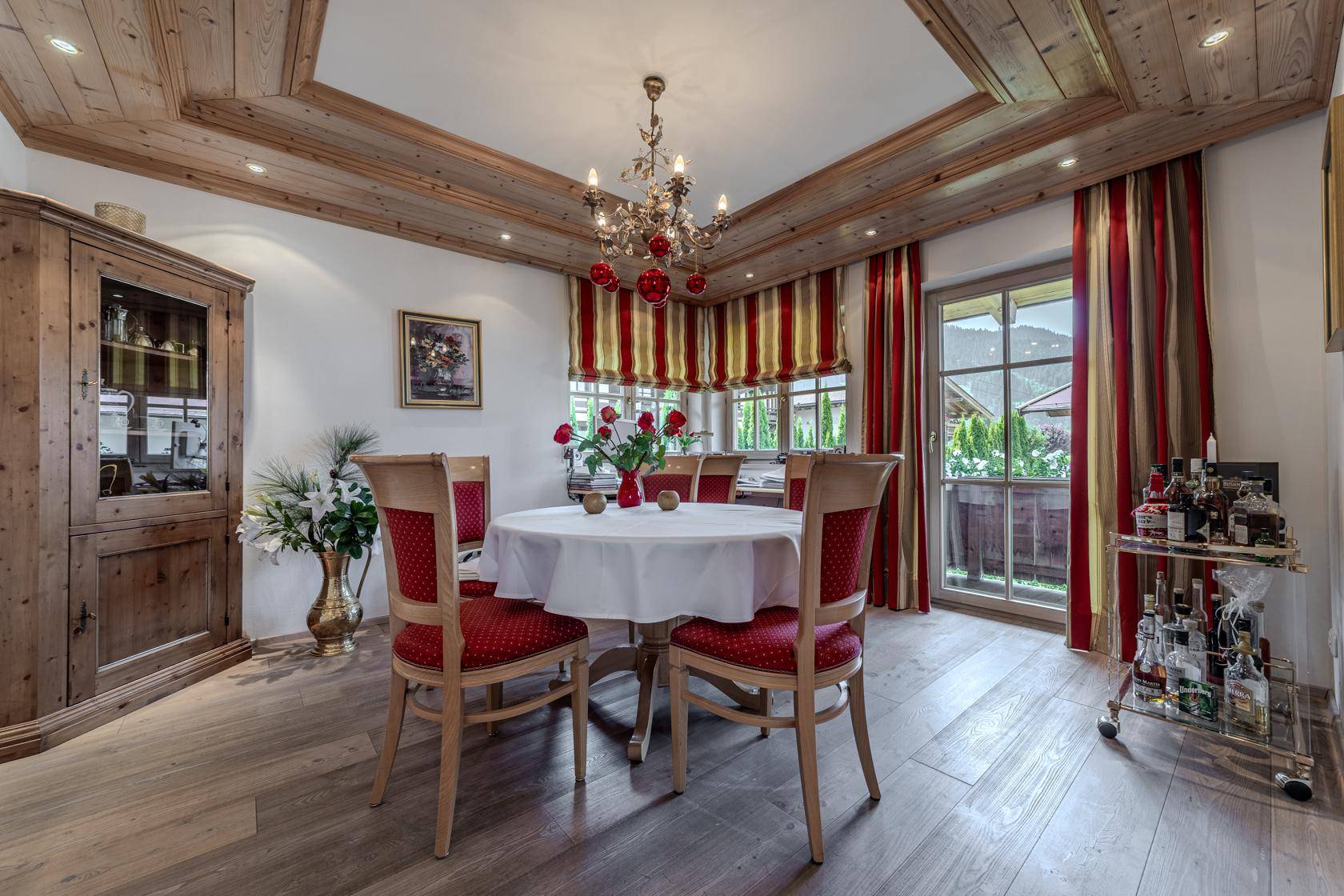 Eleganter Essbereich mit Holzbalkendecke, Kronleuchter und Zugang zum Außenbereich.
