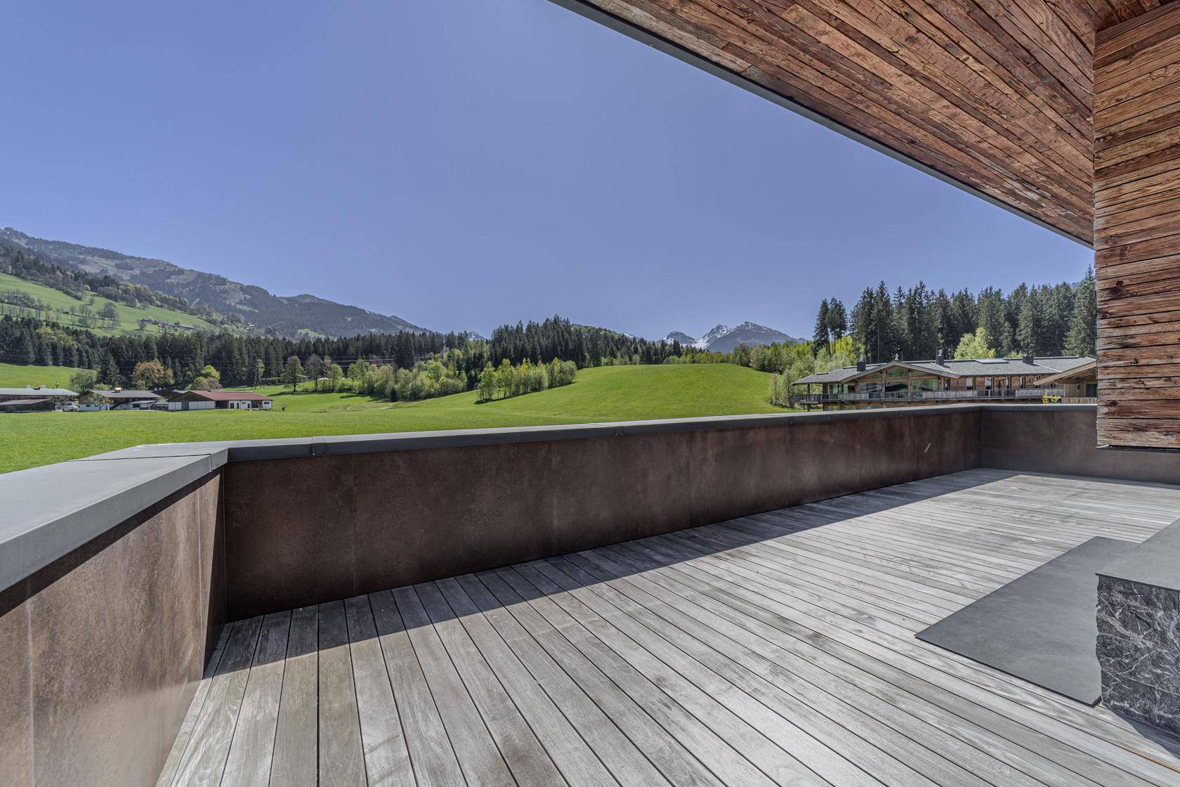 Große, offene Terrasse mit Holzboden und unverbautem Blick auf grüne Wiesen und Berge.