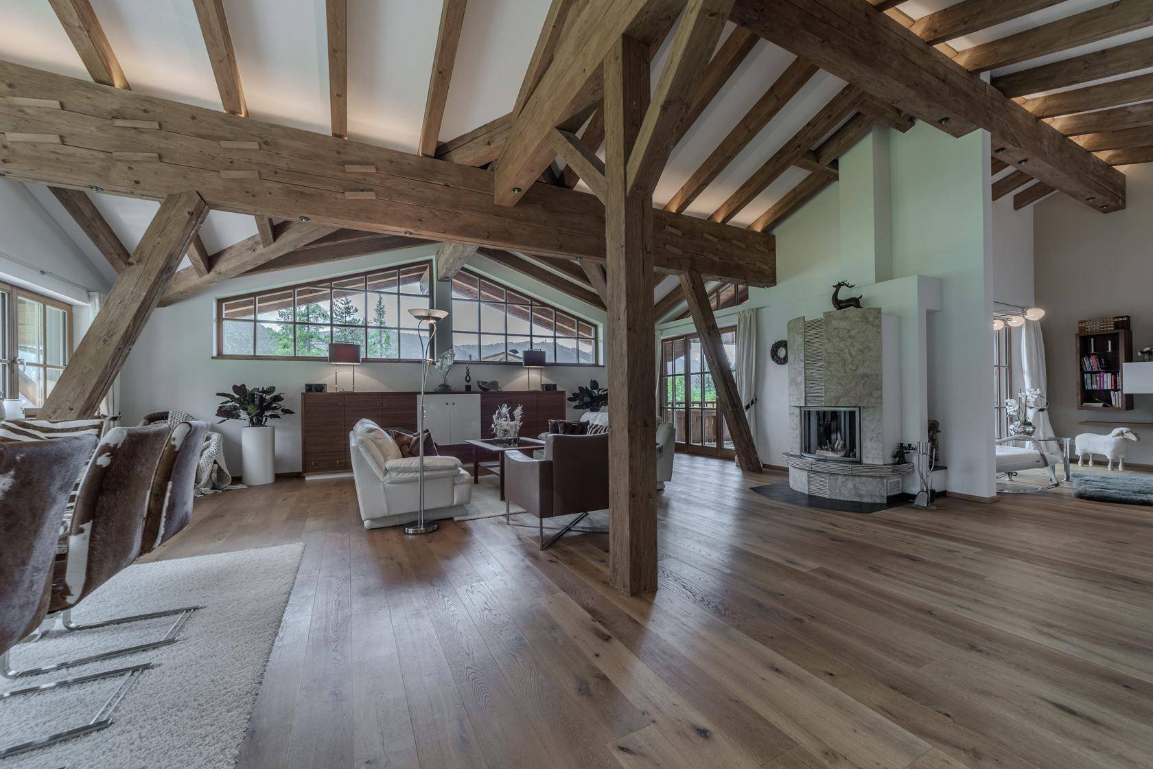 Geräumiges Wohnzimmer im alpinen Stil mit Holzbalken, Kamin und großen Fenstern mit Bergblick.