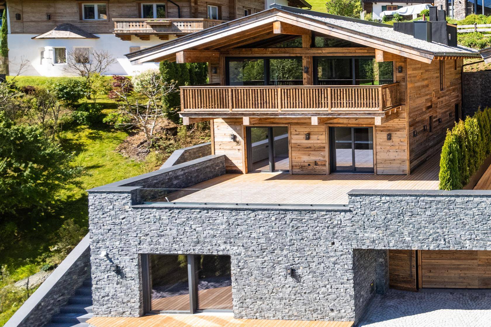 Elegantes Chalet mit Holzfassade, Steinelementen und großer Terrasse in Hanglage.