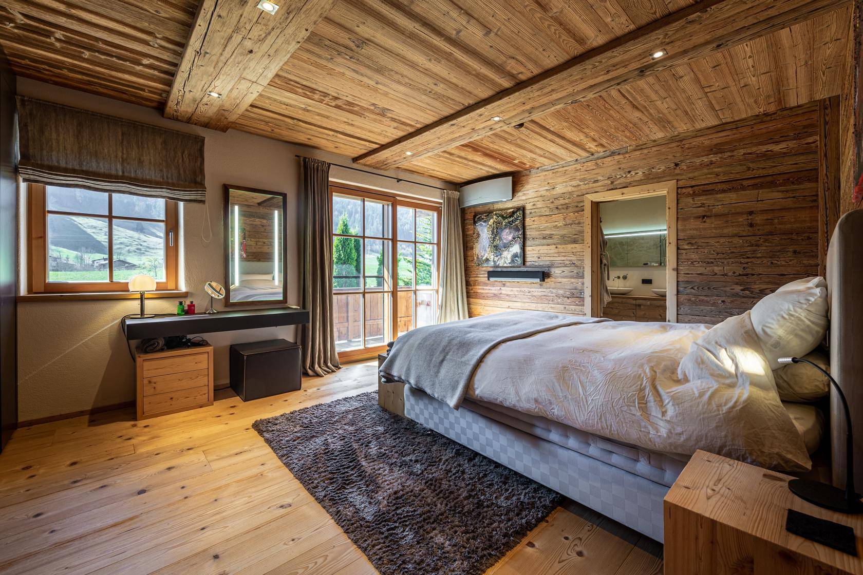 Gemütliches Schlafzimmer mit Holzwänden, Holzboden und Zugang zu einem Balkon mit Aussicht.