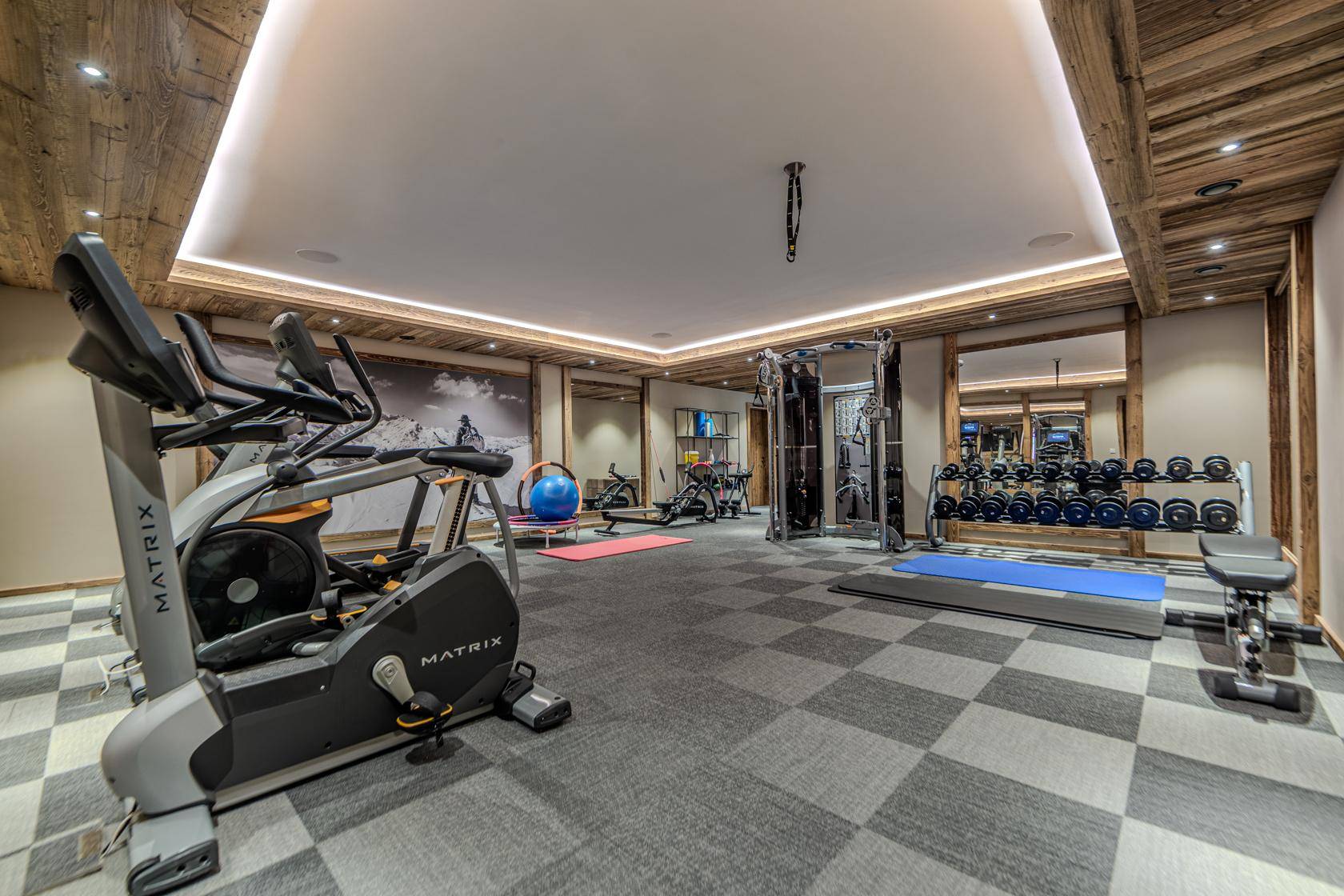 Gut ausgestatteter Fitnessraum mit verschiedenen Trainingsgeräten und Spiegelflächen.