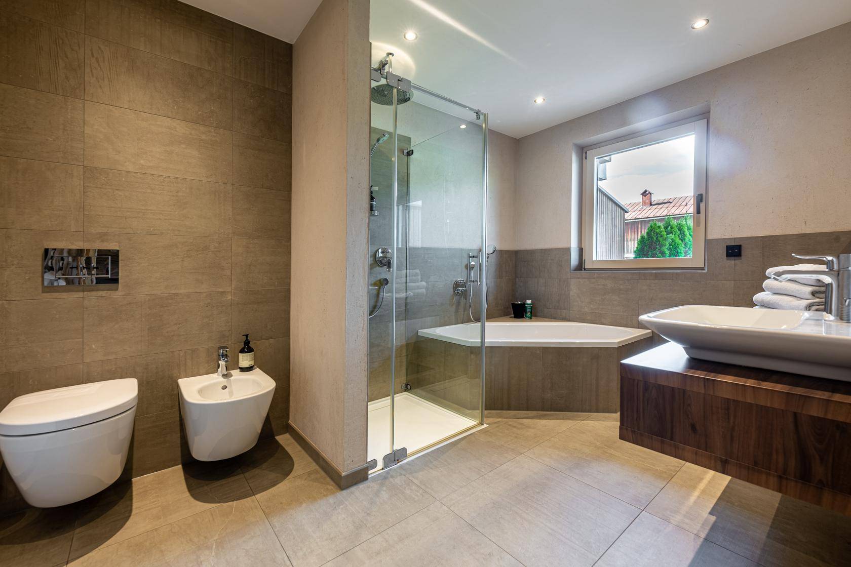 Modernes Badezimmer mit großer Dusche, Badewanne, Bidet und Fenster für Tageslicht.