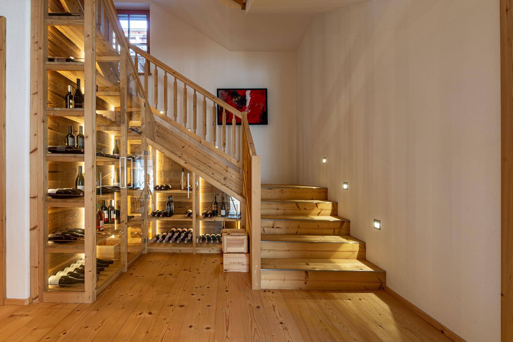 Beeindruckender Weinkeller unter der Treppe mit beleuchteten Regalen und Holztreppe.