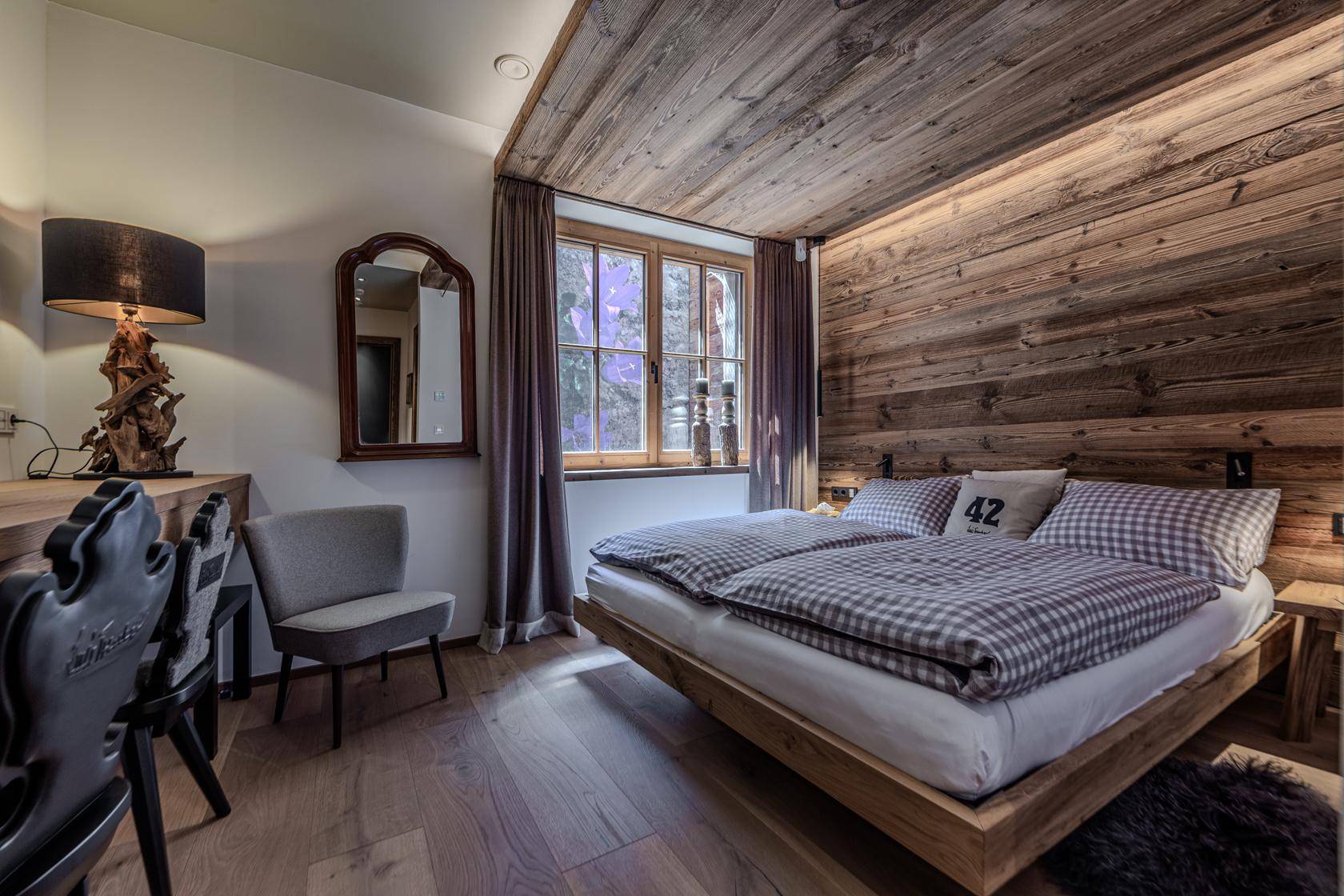 Gemütliches Schlafzimmer mit Holzwand, Holzbalkendecke und einem Fenster für natürliches Licht.