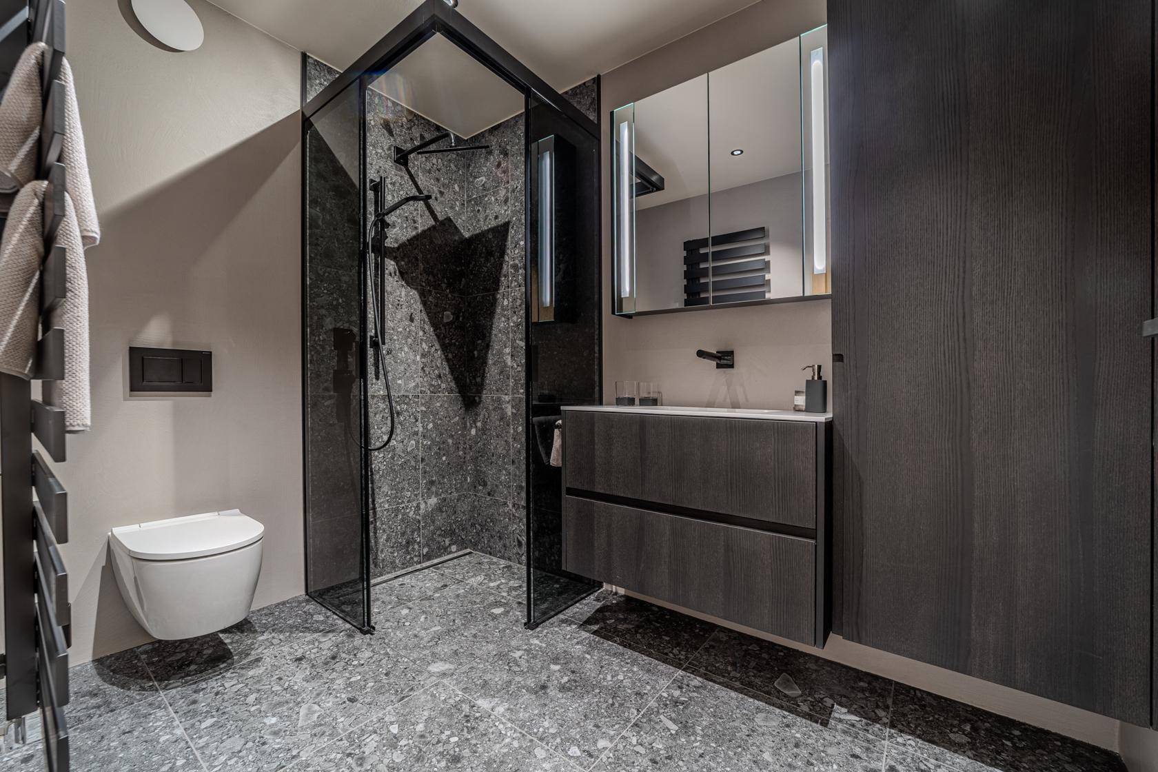 Modernes Badezimmer mit begehbarer Dusche, dunklen Fliesen und elegantem Waschtisch.