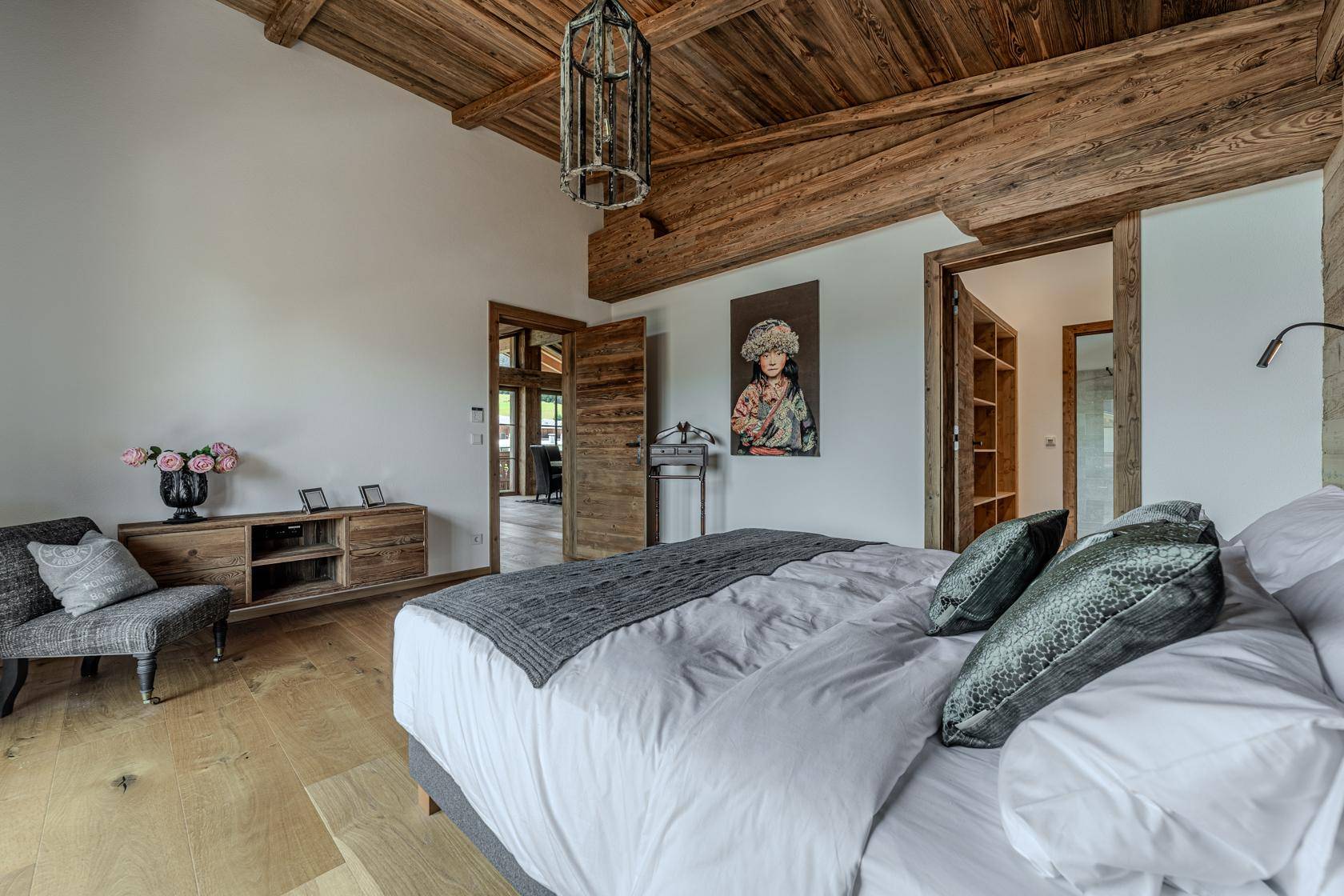 Geräumiges Schlafzimmer mit hohen Holzbalkendecken, Holzboden und Zugang zu einem weiteren Raum.