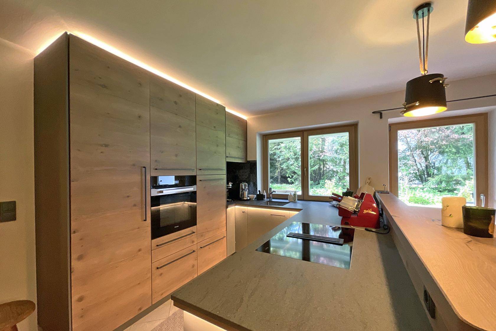 Moderne Küche mit Holzelementen, integrierten Geräten und indirekter Beleuchtung.