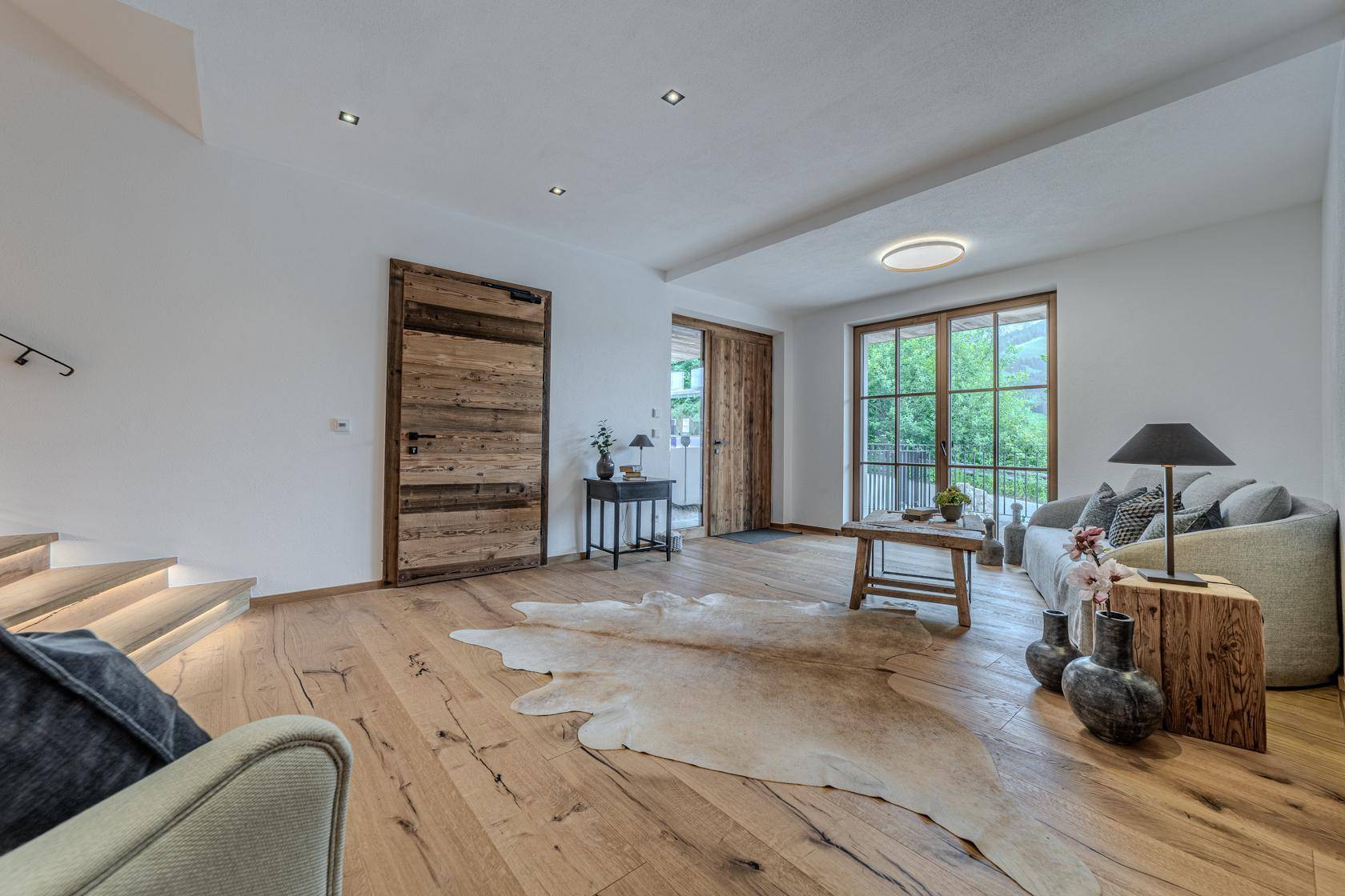 Heller Wohnbereich mit Holzboden, gemütlichem Sofa und Zugang zu einer Außenterrasse.