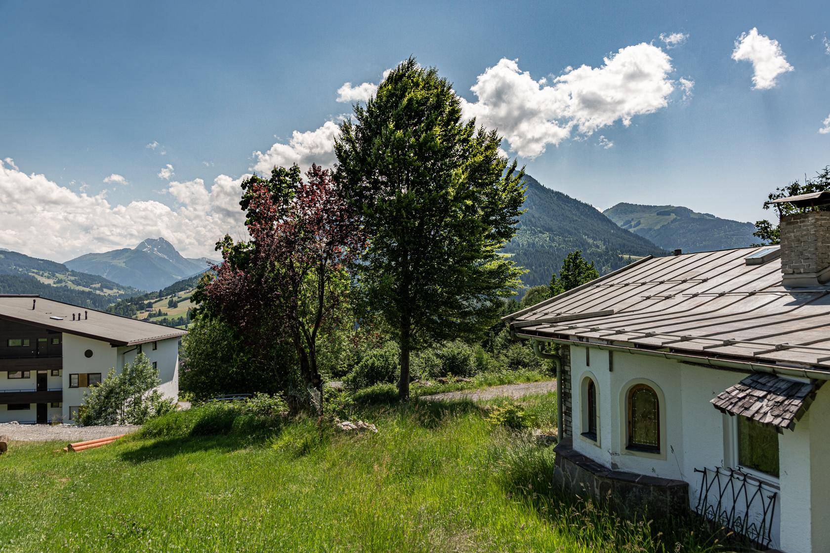 Idyllische ländliche Landschaft mit einem kleinen Haus, grünen Wiesen und majestätischen Bergen im Hintergrund.