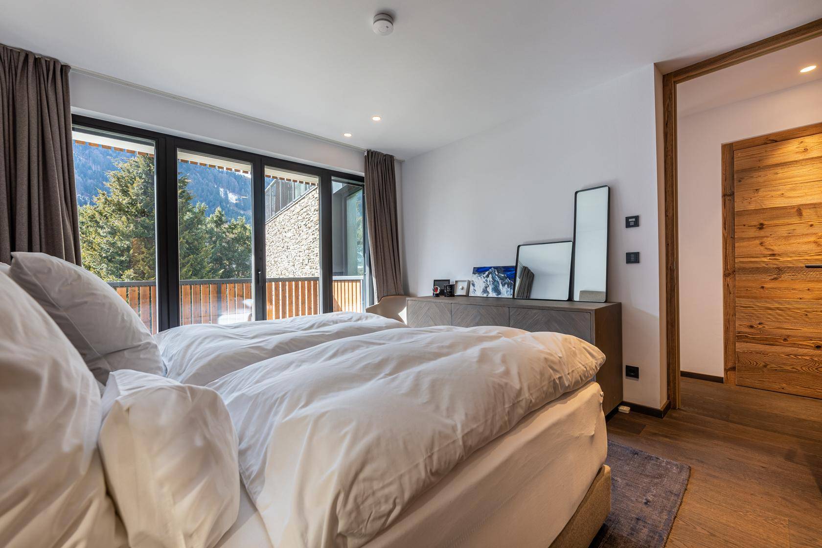 Helles Schlafzimmer mit Doppelbett, Holzboden und Balkonzugang mit Bergblick.