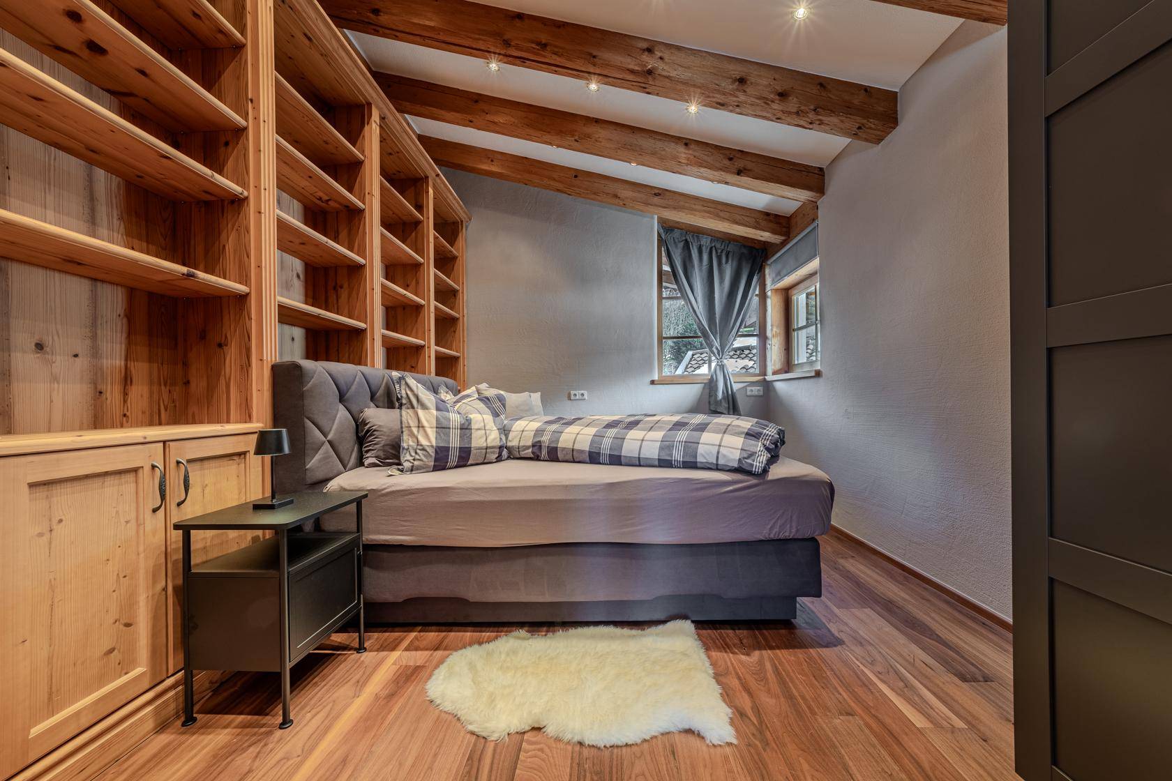 Gemütliches Schlafzimmer mit Holzbalkendecke, integrierten Bücherregalen und Holzboden.