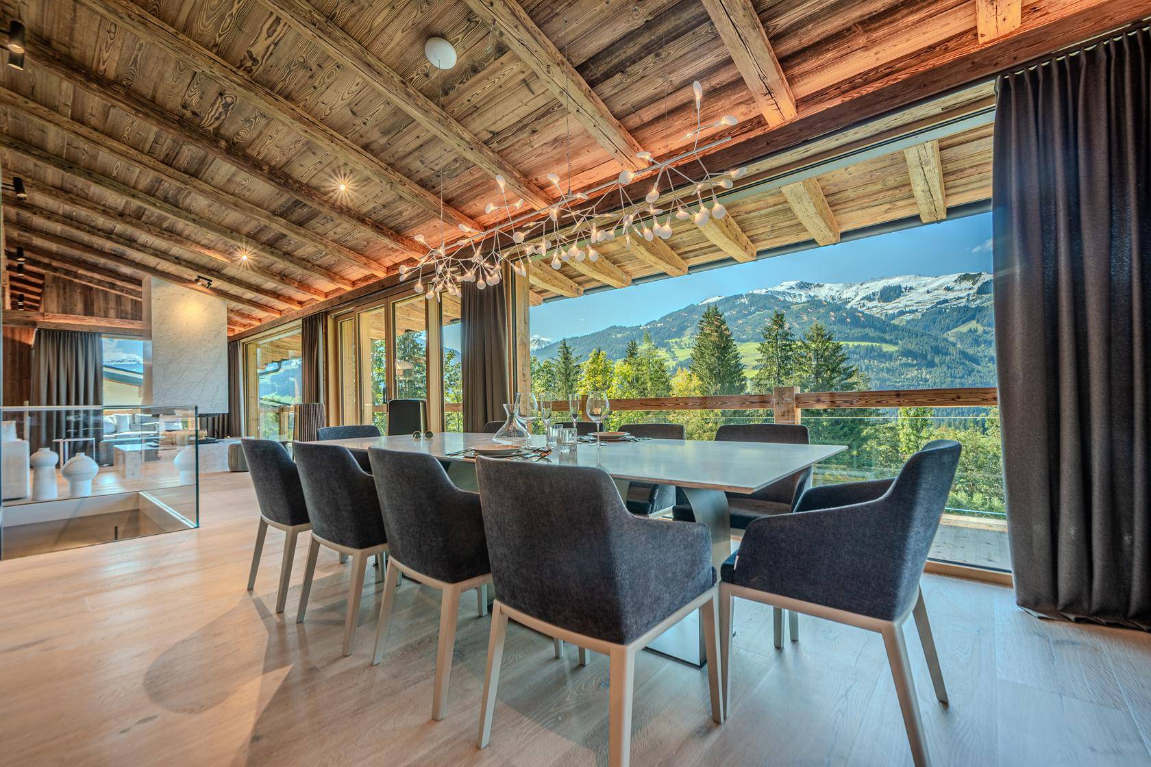 Geräumiger Wohn-Essbereich mit Kamin, Holzbalken und beeindruckendem Panoramablick auf die Berge.