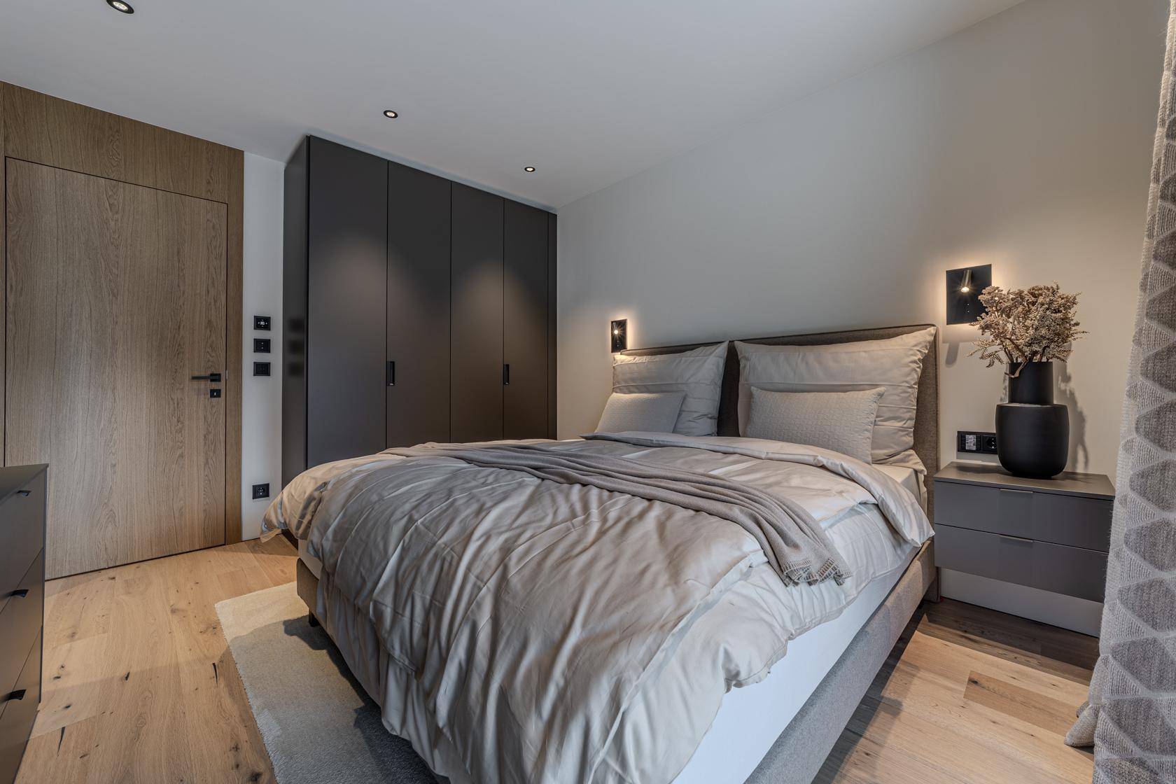 Ruhiges Schlafzimmer mit großem Bett, dunklen Einbauschränken und hellem Holzboden.