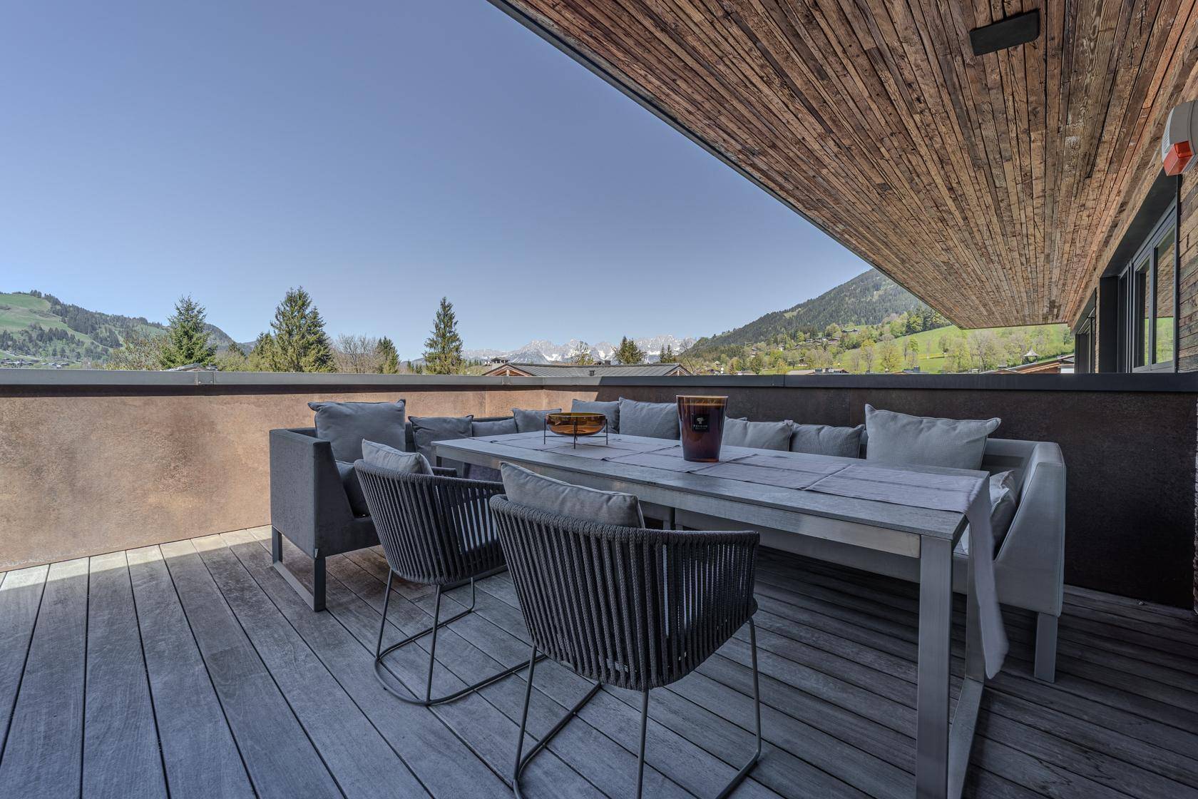 Geräumige Terrasse mit bequemen Sitzmöbeln, Holzboden und weitem Blick auf die Berge.