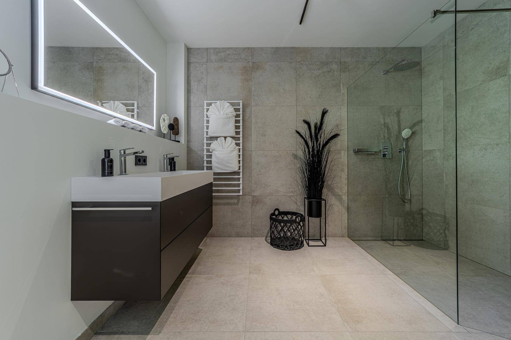 Modernes Badezimmer mit großformatigen Fliesen, Doppelwaschbecken und einer geräumigen begehbaren Dusche.