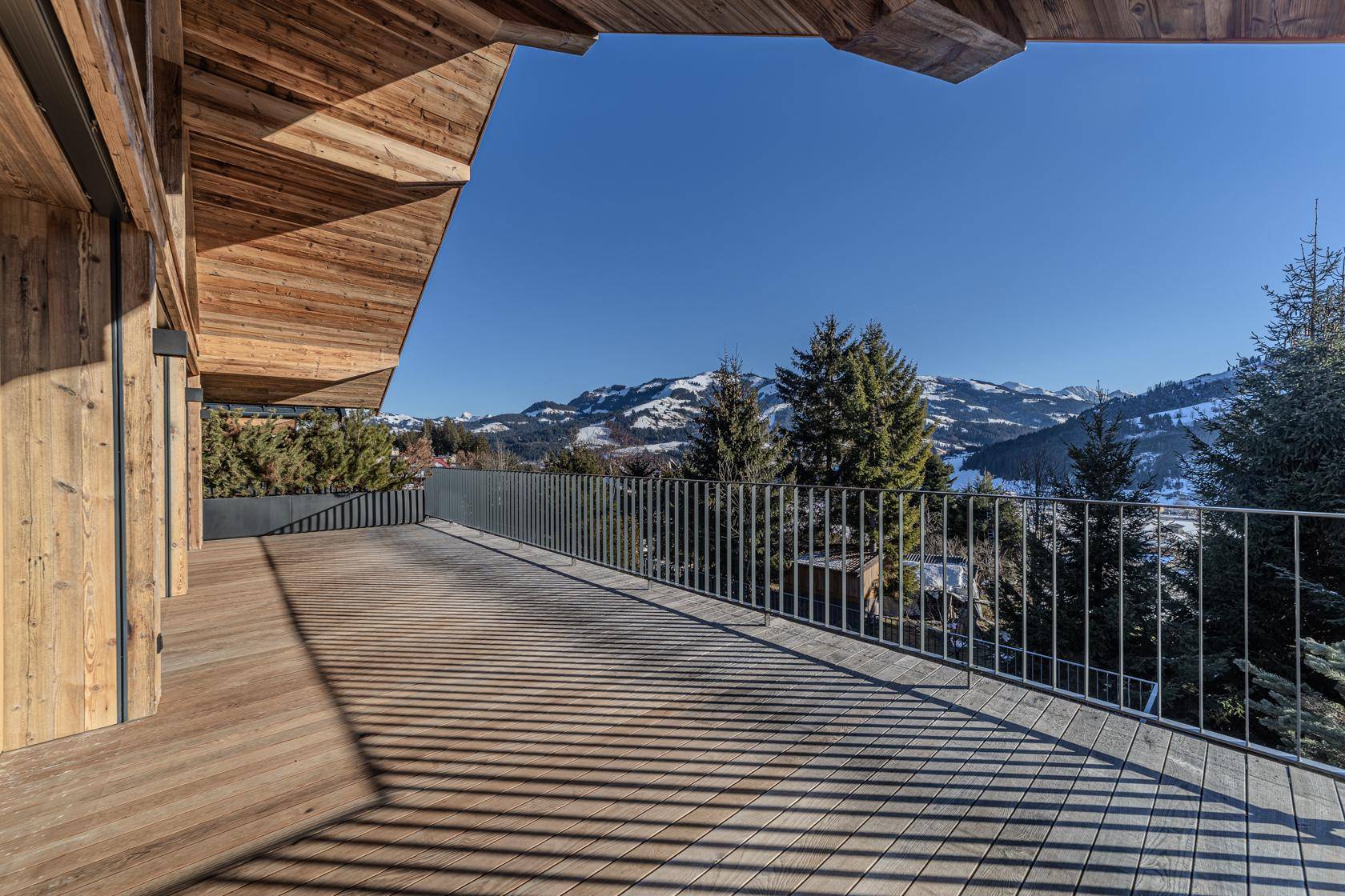 Geräumige Holzterrasse mit weitem Blick auf die schneebedeckten Berge und Wälder.