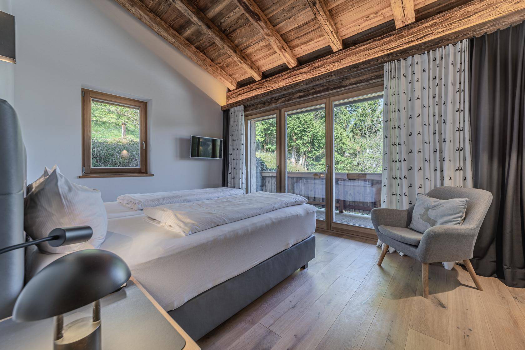 Gemütliches Schlafzimmer mit Holzbalkendecke, Balkonzugang und Blick ins Grüne.