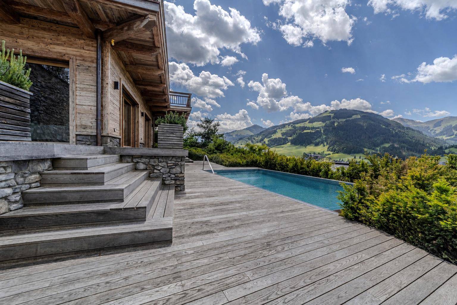 Luxuriöses Holzchalet mit Infinity-Pool und atemberaubendem Bergblick unter blauem Himmel.