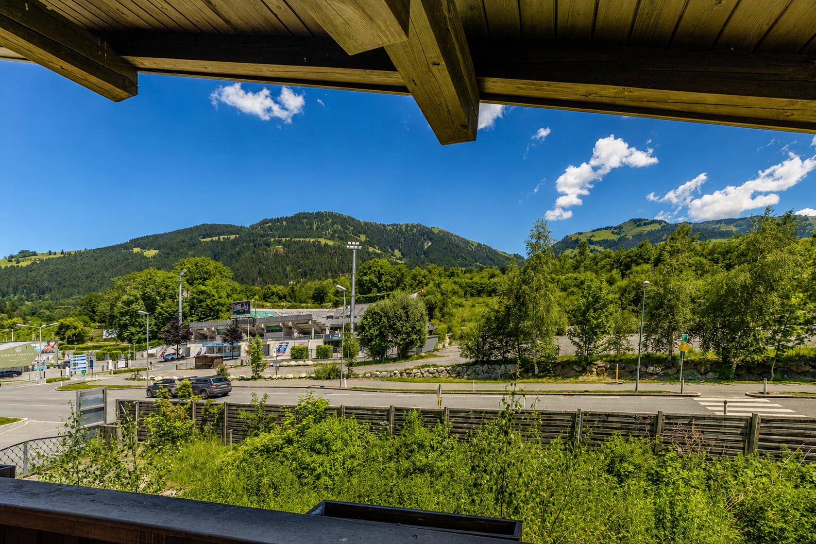 Blick von einem Balkon auf die umliegende Landschaft mit Straße, Gebäuden und Bergen im Hintergrund.