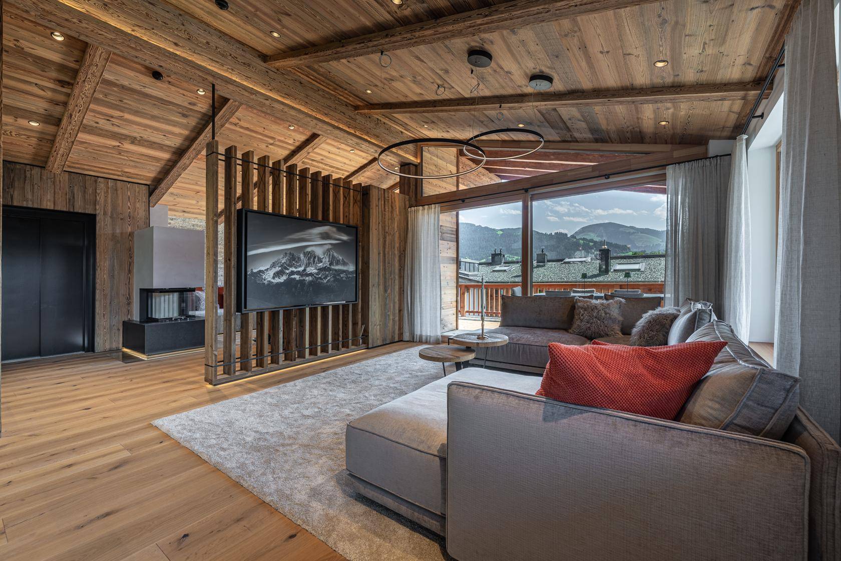 Helles Wohnzimmer mit Holzboden, bequemer Couch und Panoramafenstern mit Bergblick.