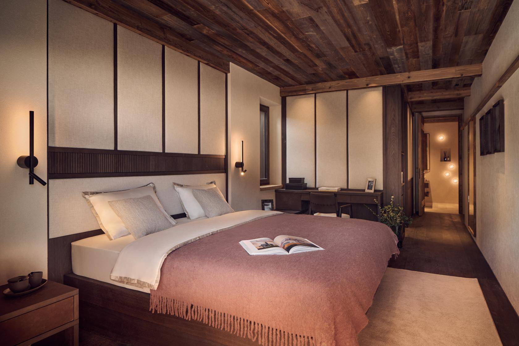 Ruhiges Schlafzimmer mit Holzbalkendecke, großem Bett und integriertem Schreibtischbereich.