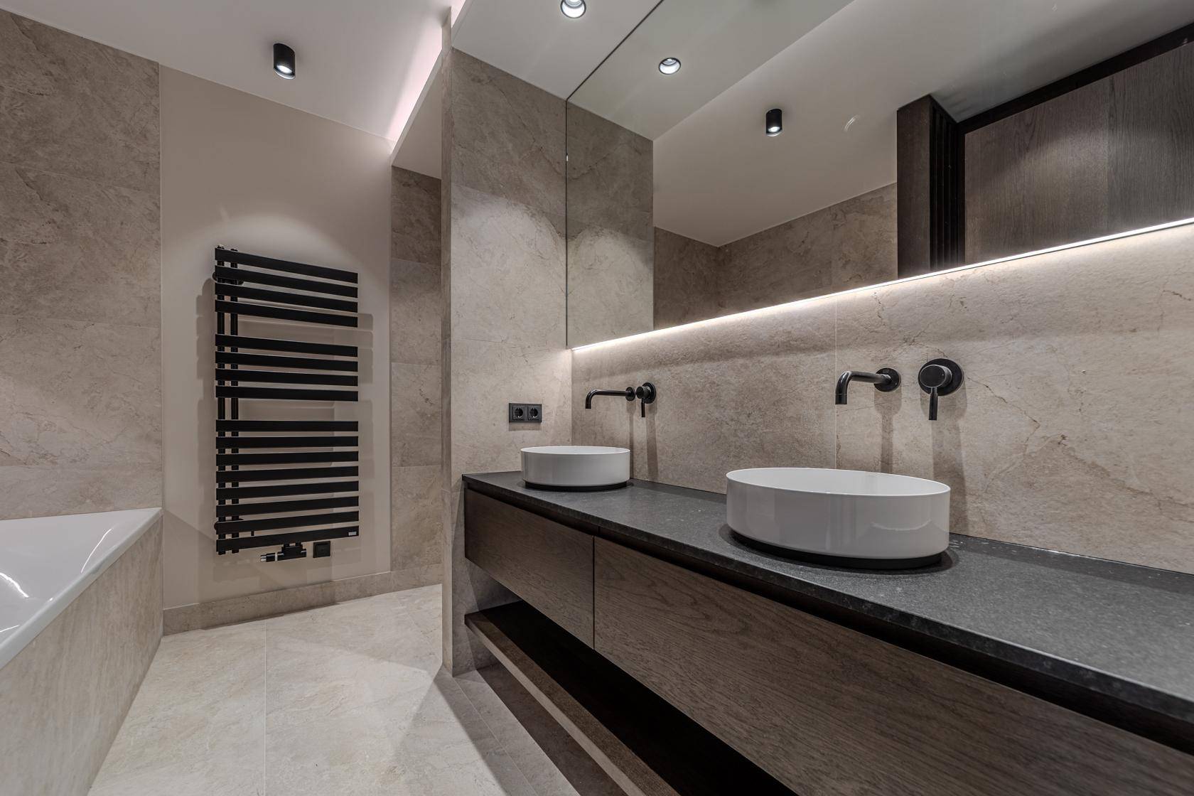 Elegantes Badezimmer mit Doppelwaschbecken, großem Spiegel, beheiztem Handtuchhalter und modernen Fliesen.