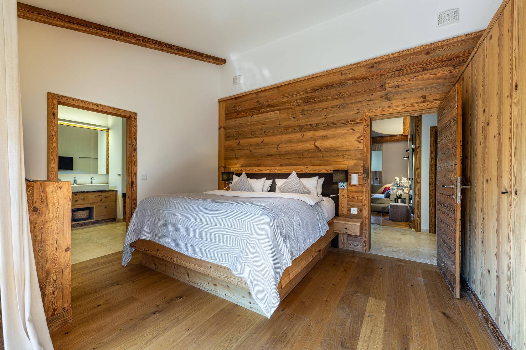 Schlafzimmer im alpinen Stil mit Holzwänden, Holzboden und direktem Zugang zum Badezimmer.