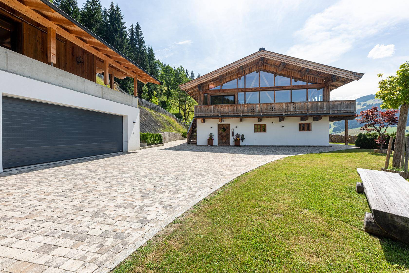 Zufahrt zum Haus mit Doppelgarage und gepflegtem Vorgarten in alpiner Landschaft.