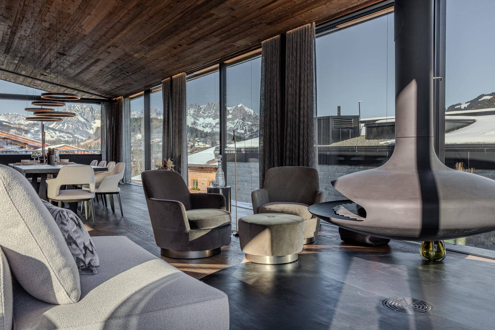 Stilvolles Wohnzimmer mit freistehendem Kamin, Sesseln und Panoramafenstern mit Bergblick.