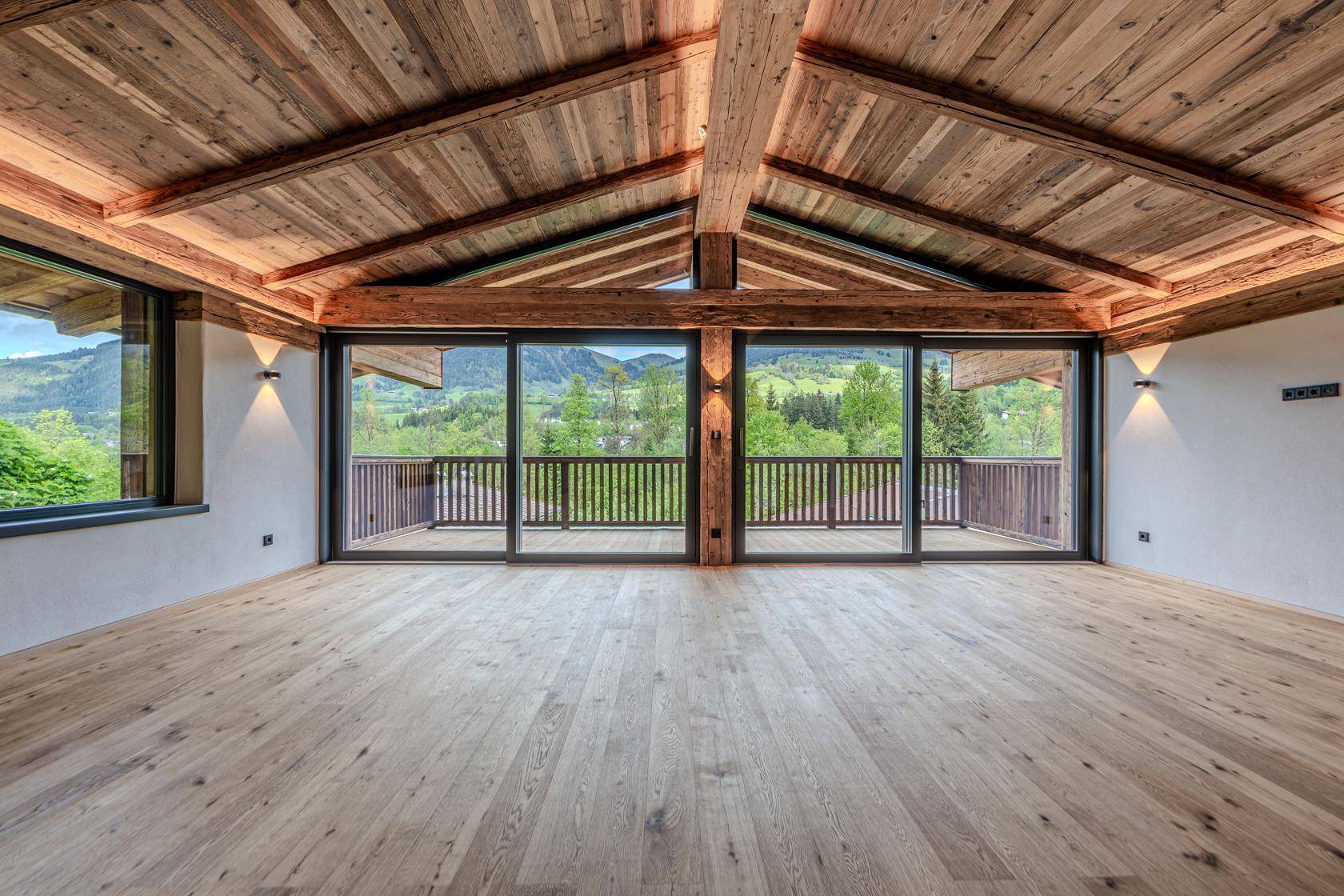 Heller Wohnbereich mit Holzboden, hohen Decken und Zugang zu einem Balkon mit Bergblick.