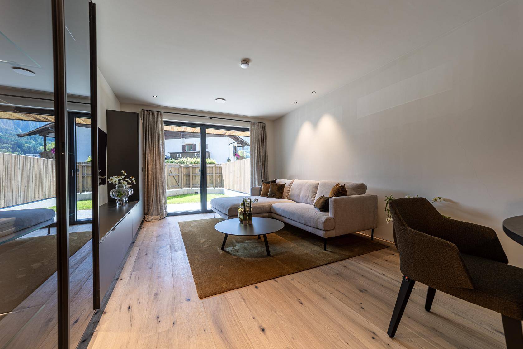 Helles Wohnzimmer mit beigem Sofa, Holzboden und direktem Zugang zu einem kleinen Gartenbereich.