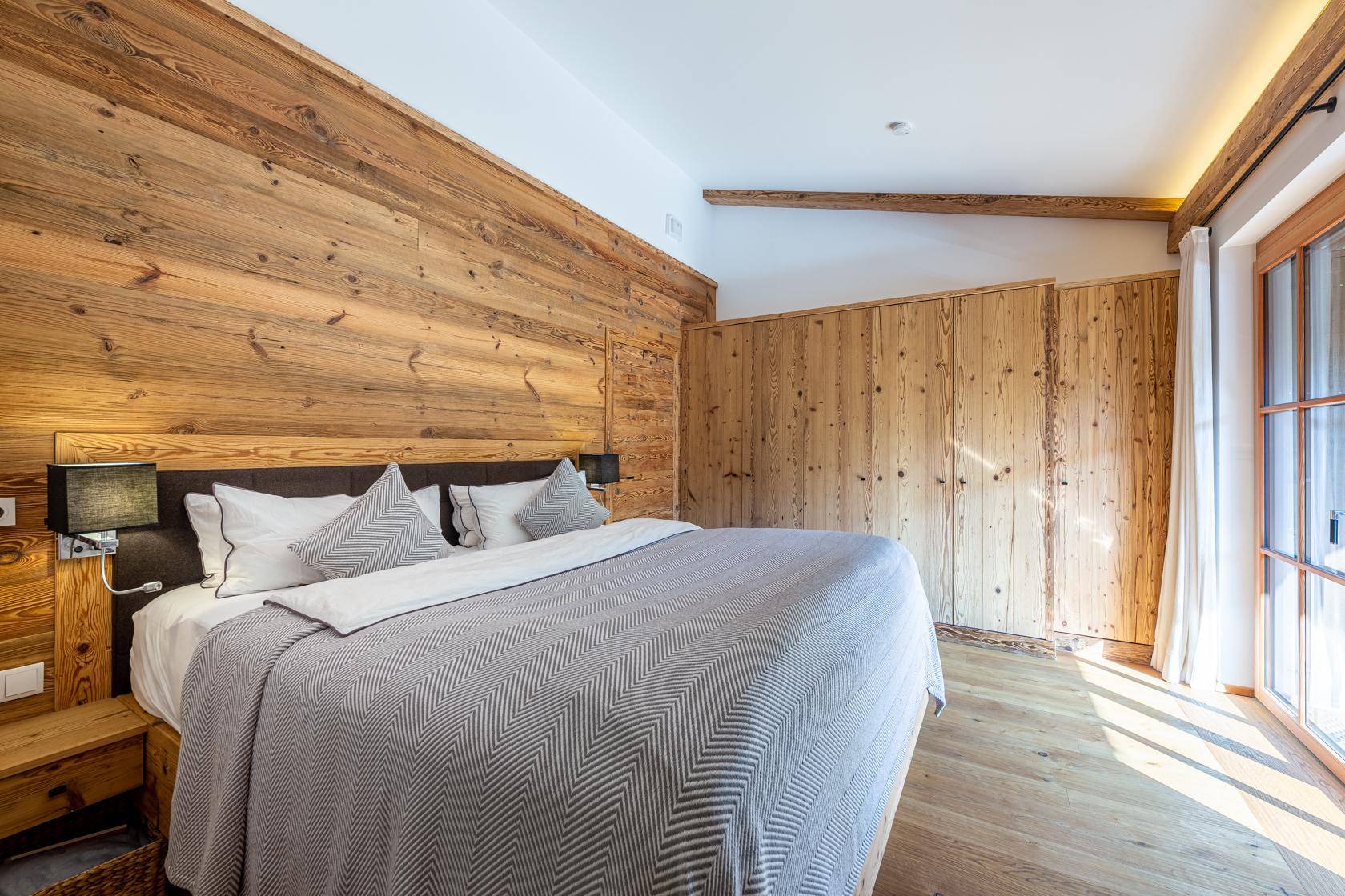 Schlafzimmer im alpinen Stil mit Holzwänden, Holzboden und viel Tageslicht durch die Terrassentür.