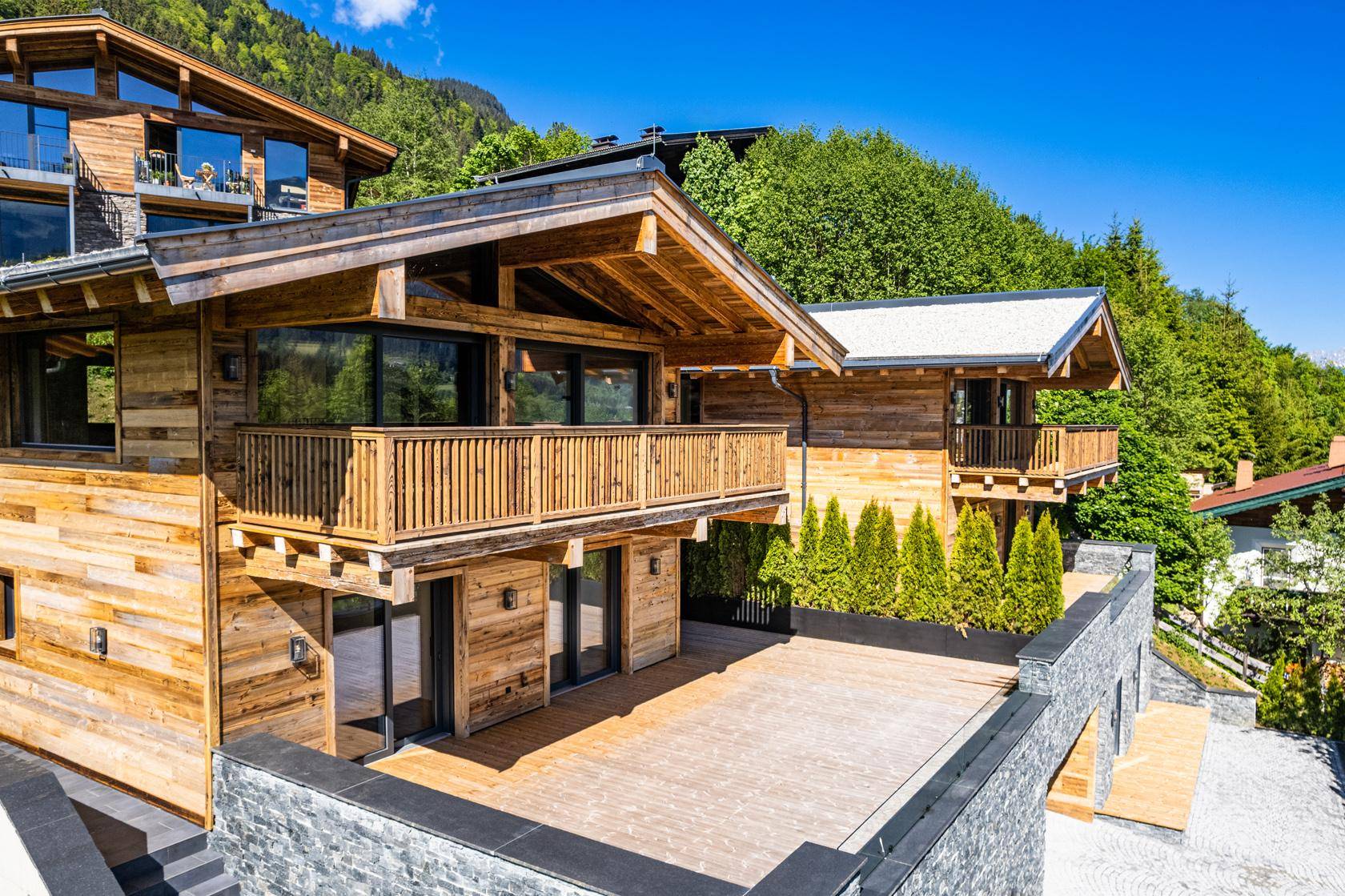 Luxuriöse Chalets in alpiner Umgebung mit Holzfassaden und Steinelementen, eingebettet in grüne Hügel.