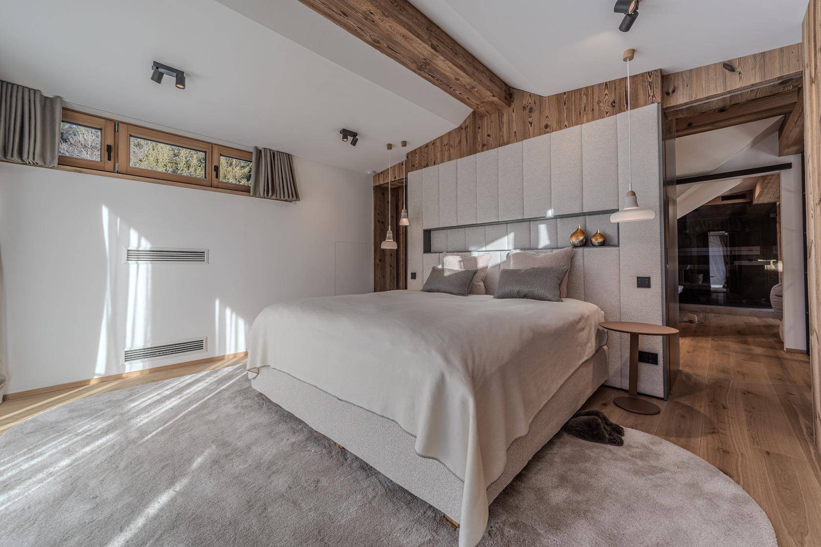 Helles Schlafzimmer mit Doppelbett, Holzwänden und indirekter Beleuchtung unter Holzbalken.